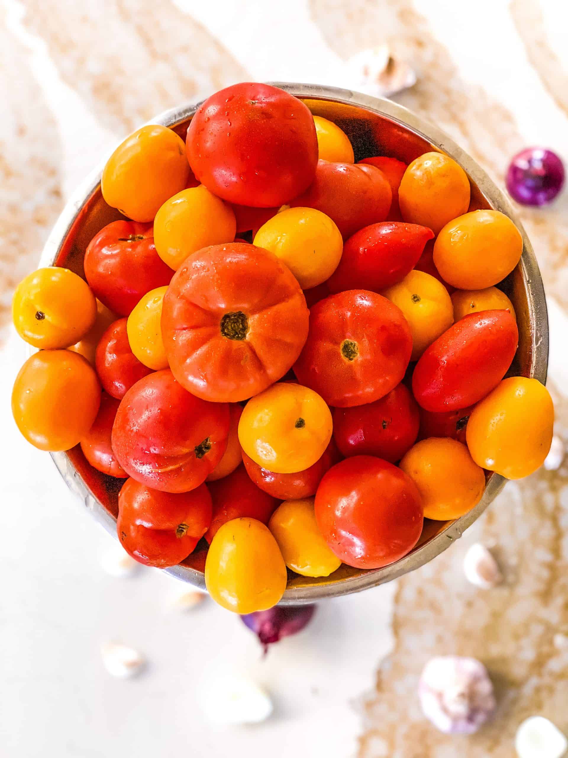 A bowl full of red and yellow tomatoes with garlic in the foreground.