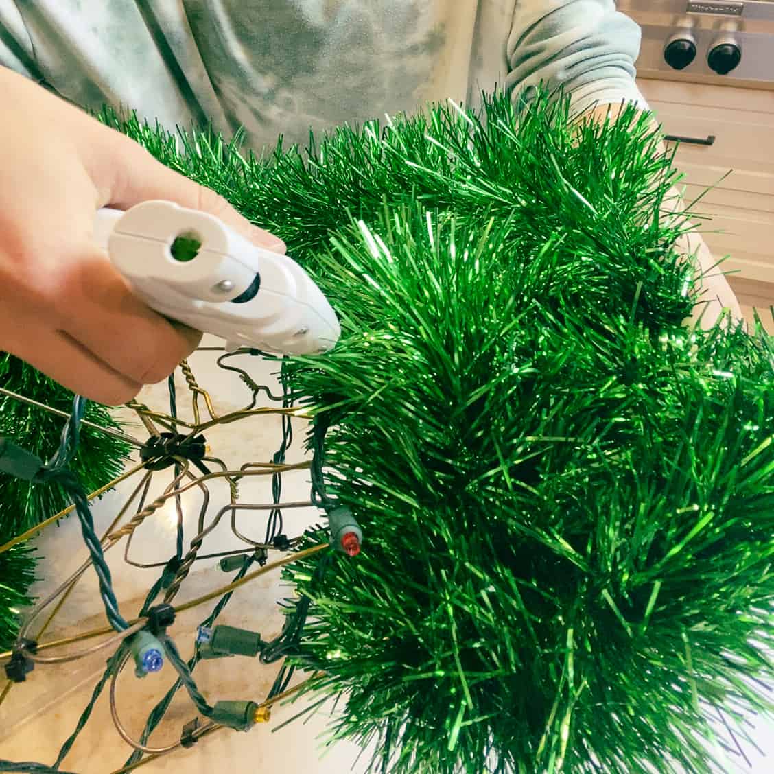 Using a hot glue gun to attach the garland to the wire hanger Christmas tree.