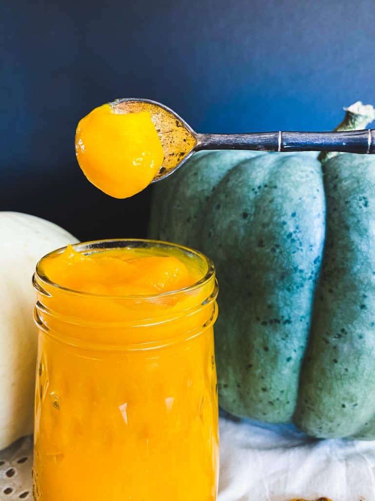 Thick homemade pumpkin puree on a spoon above a jar.