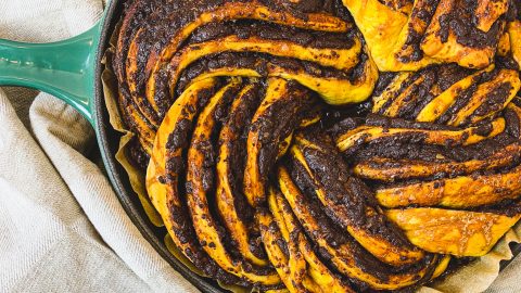 Overhead view of Pumpkin Chocolate Babka sitting inside of a cast iron pan. Chocolate swirls and orange coloured bread.