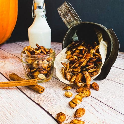 Sweet and Salty chai spiced pumpkin seeds spilling out of an old cream can with cinnamon sticks, milk, and a pumpkin in the background.