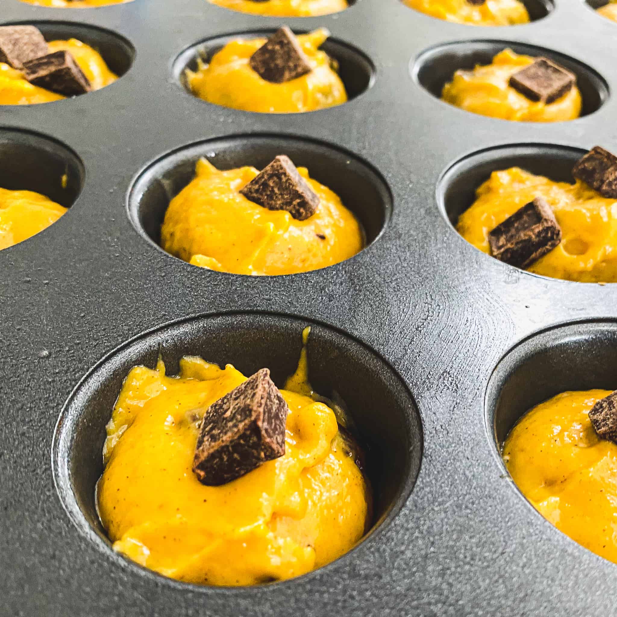 Mini pumpkin chocolate chunk muffins uncooked with extra chunks of chocolate sprinkled over top.