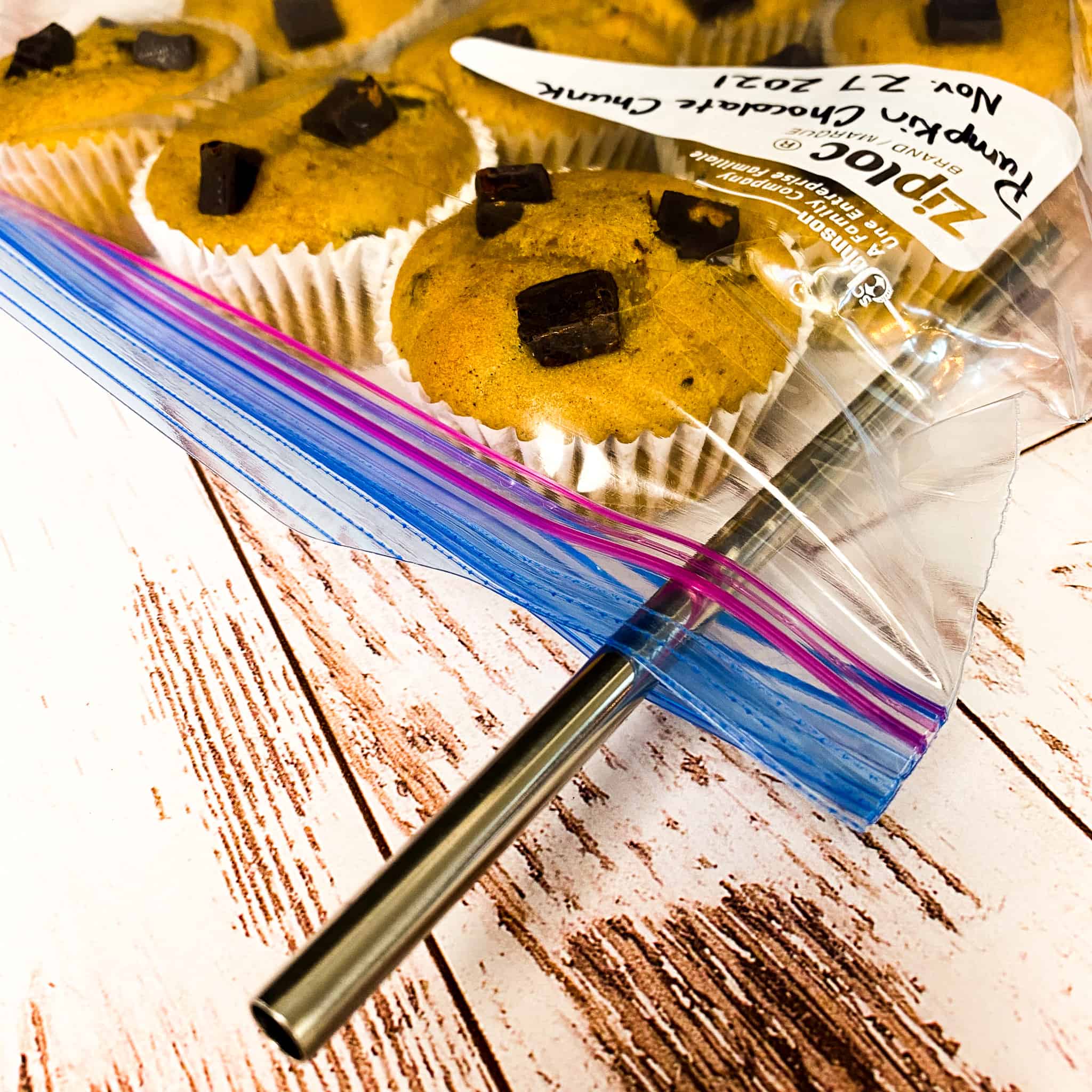A straw inserted into a large ziplock bag full of muffins, ready to suck all of the air out.