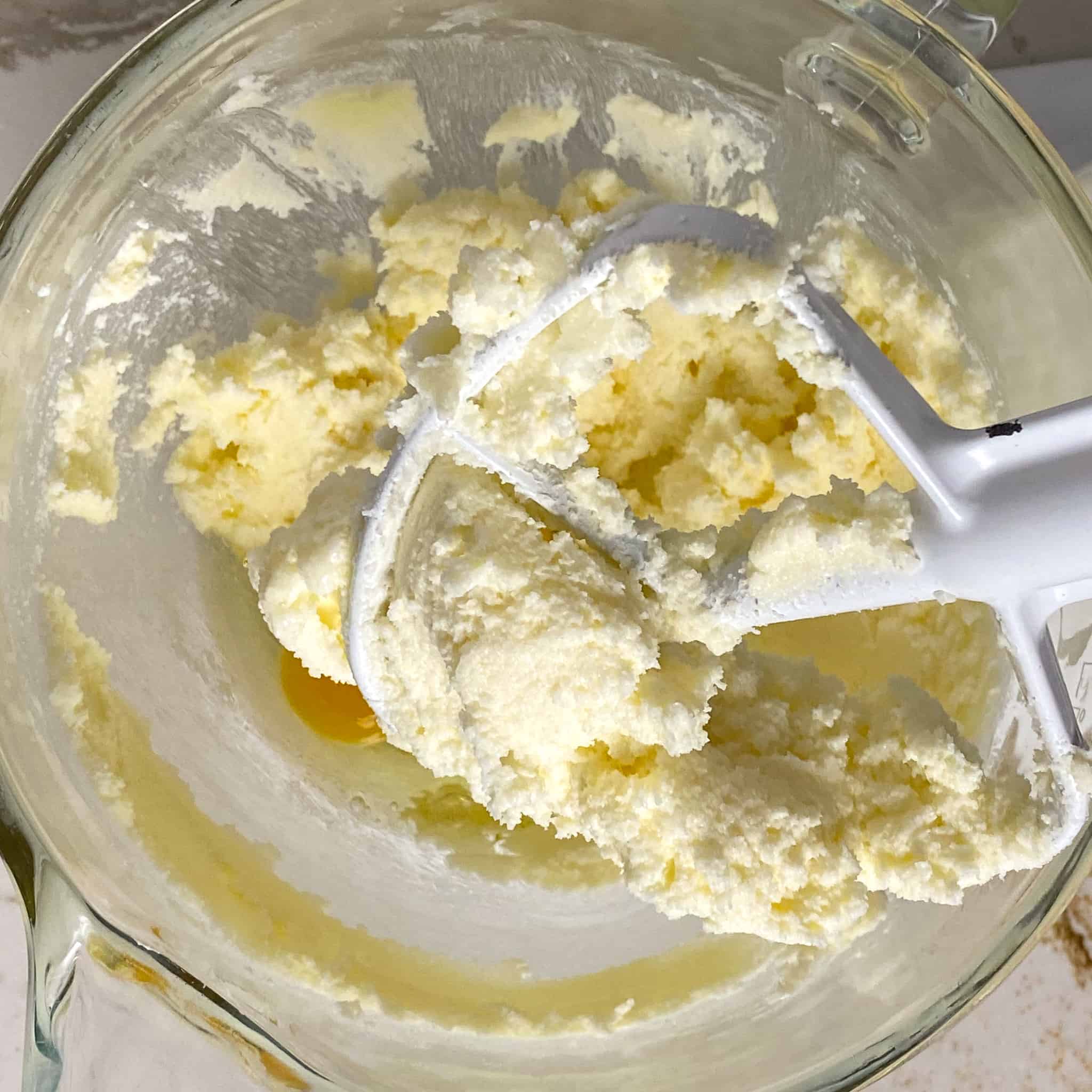 Butter and sugar creamed in a glass mixing bowl with a white kitchenaid paddle attachment in the mix.