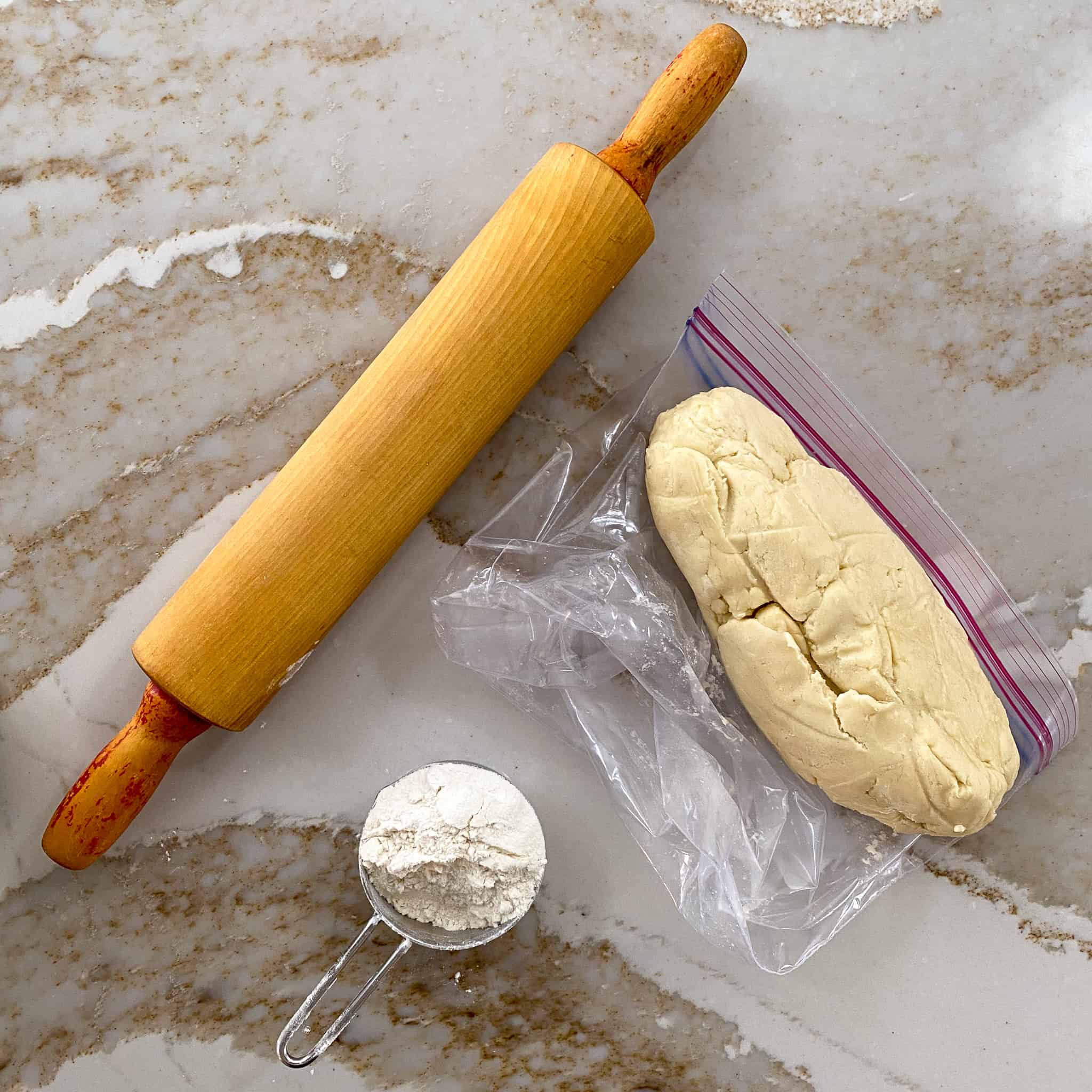 Rolling pin, dusting flour, and chilled cookie dough sitting on the counter ready to roll out.