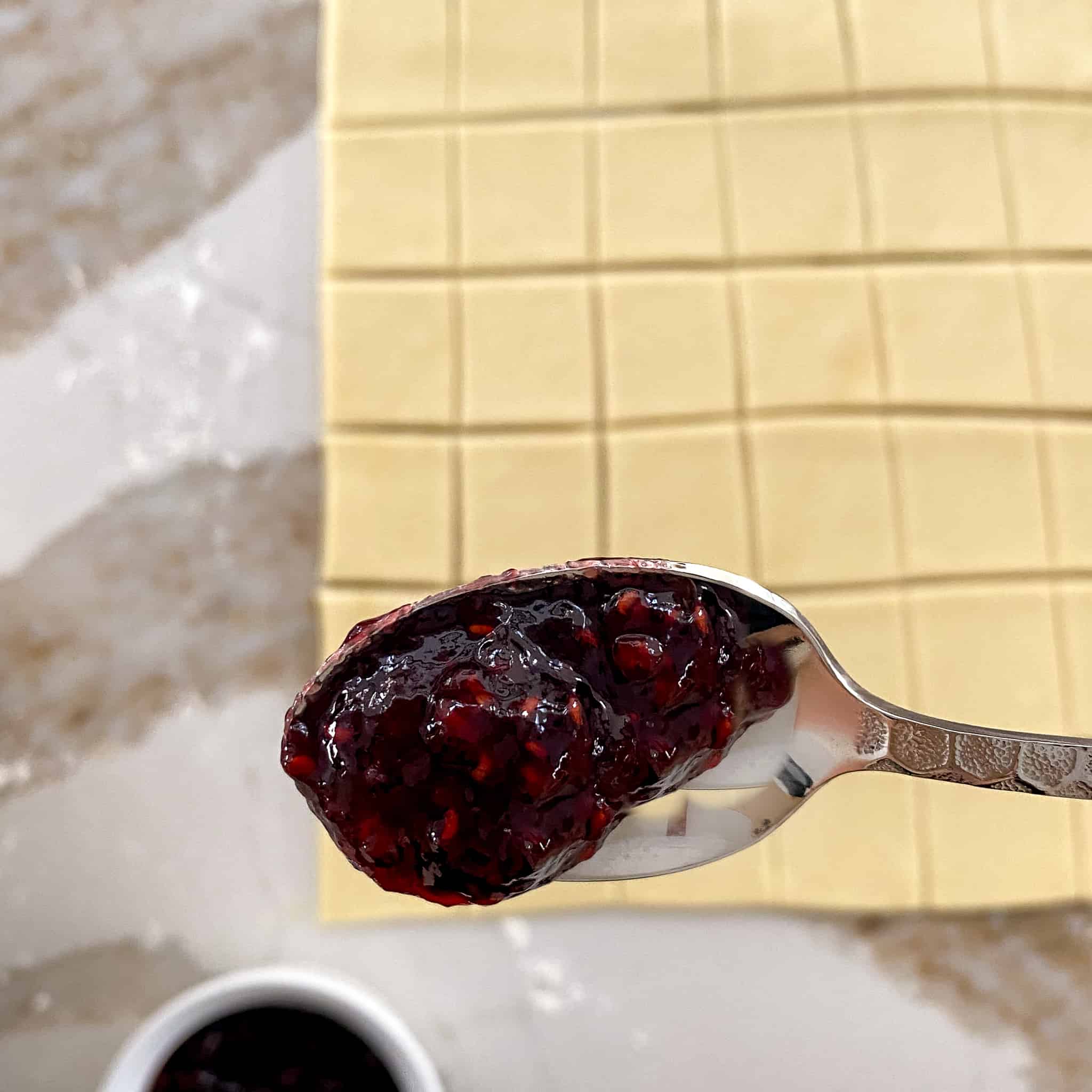 Thick raspberry jam staying on a tipped spoon above cut up dough.