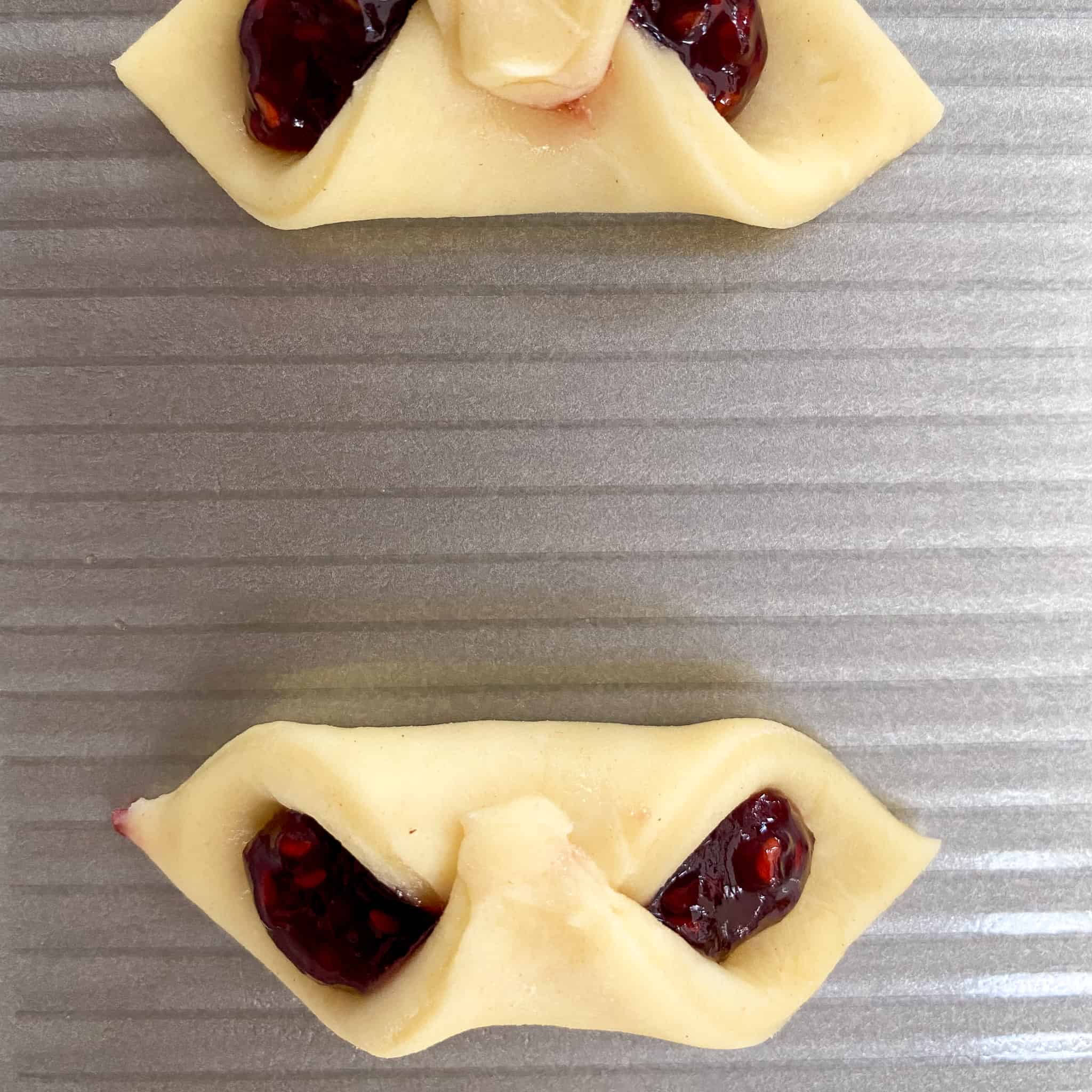 Two kolaczki cookies folded and filled with raspberry jam.