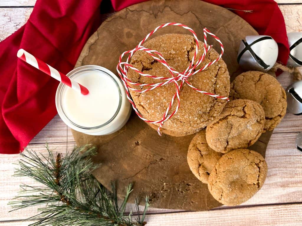 Old fashioned ginger snap cookies tied up with red and white string and piled on top of a wooden slab with a silver bell and sprig of spruce.