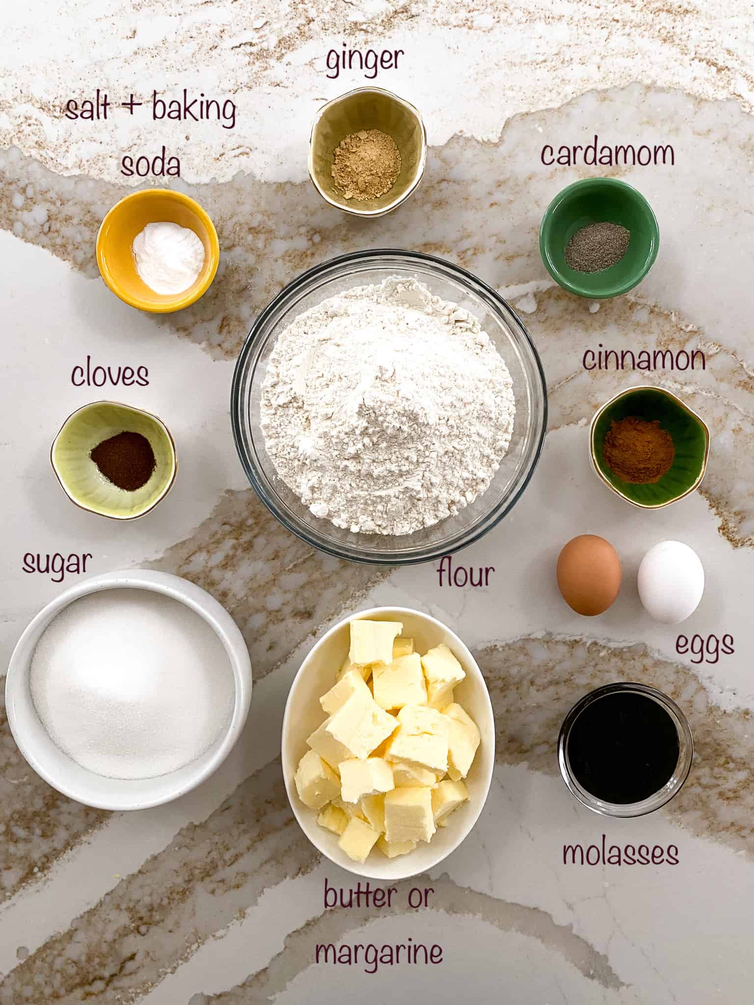 Key ingredients overhead view including flour, cloves, cardamom, cinnamon, ginger, baking soda, salt, sugar, butter, molasses.