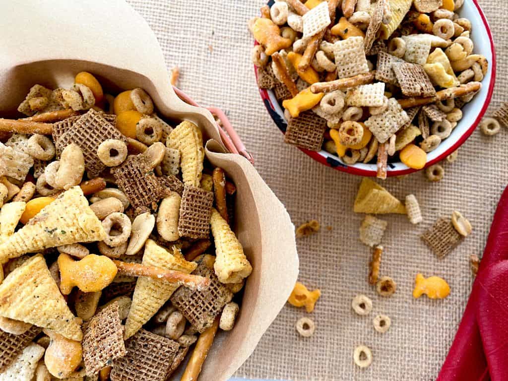 Smoked Ranch Chex mix wrapped in parchment in a bowl. Chex mix pieces spilling out onto the floor.