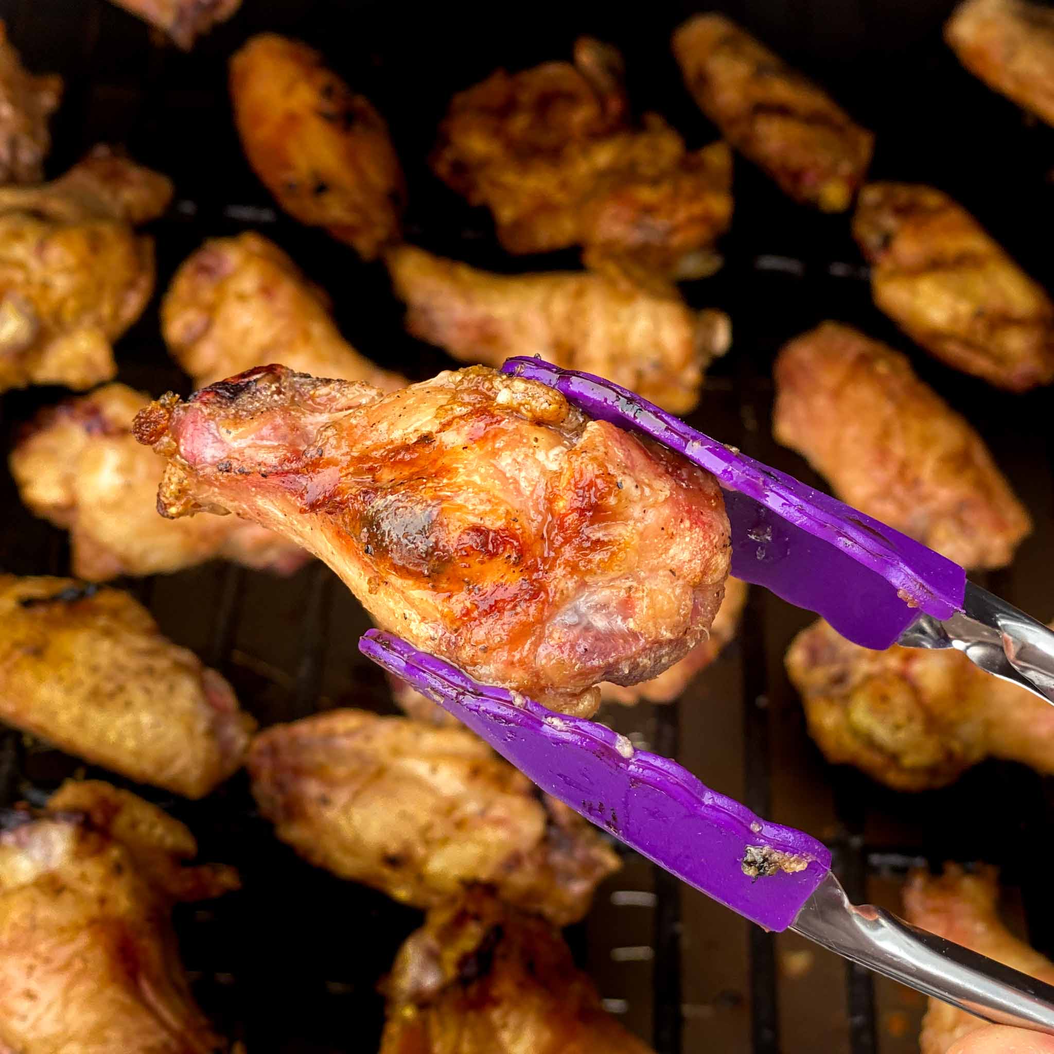 A brined chicken wing with crispy skin being held up over a pellet grill.
