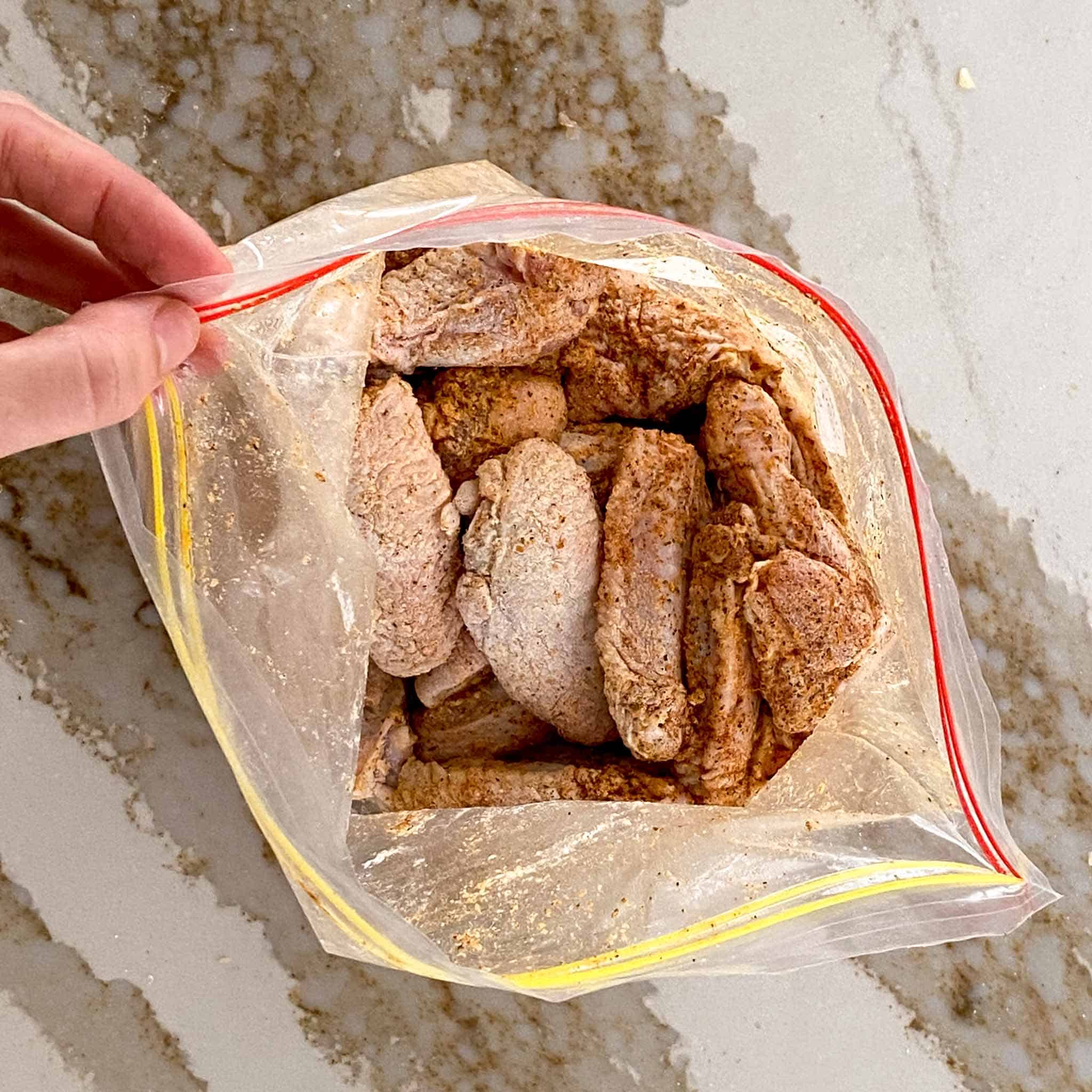 Raw chicken wings being seasoned in a large ziplock bag.