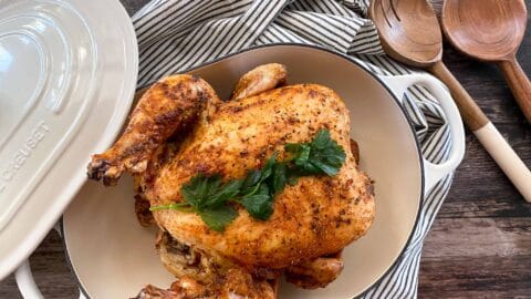 Smoked beer can chicken in a casserole dish with parsley placed on top for garnish.