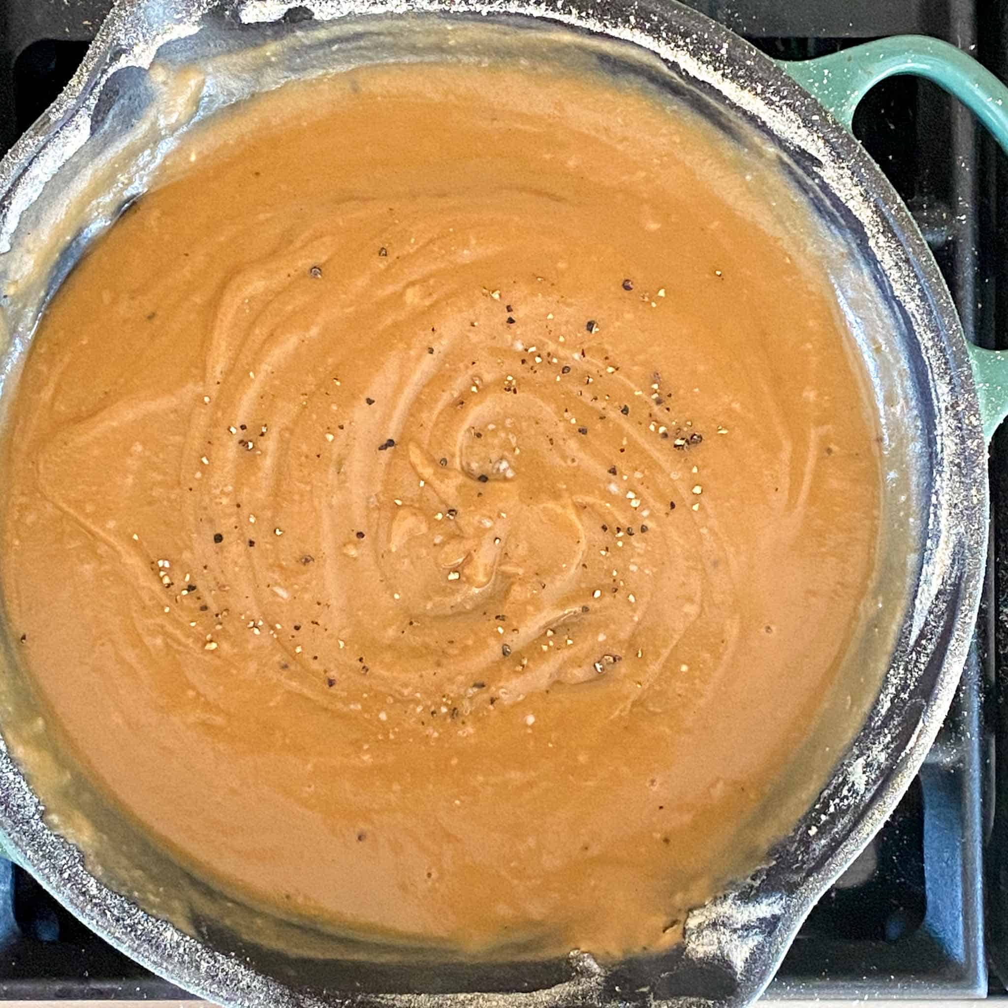 Gravy in a cast iron pan with salt and pepper sprinkled on top.