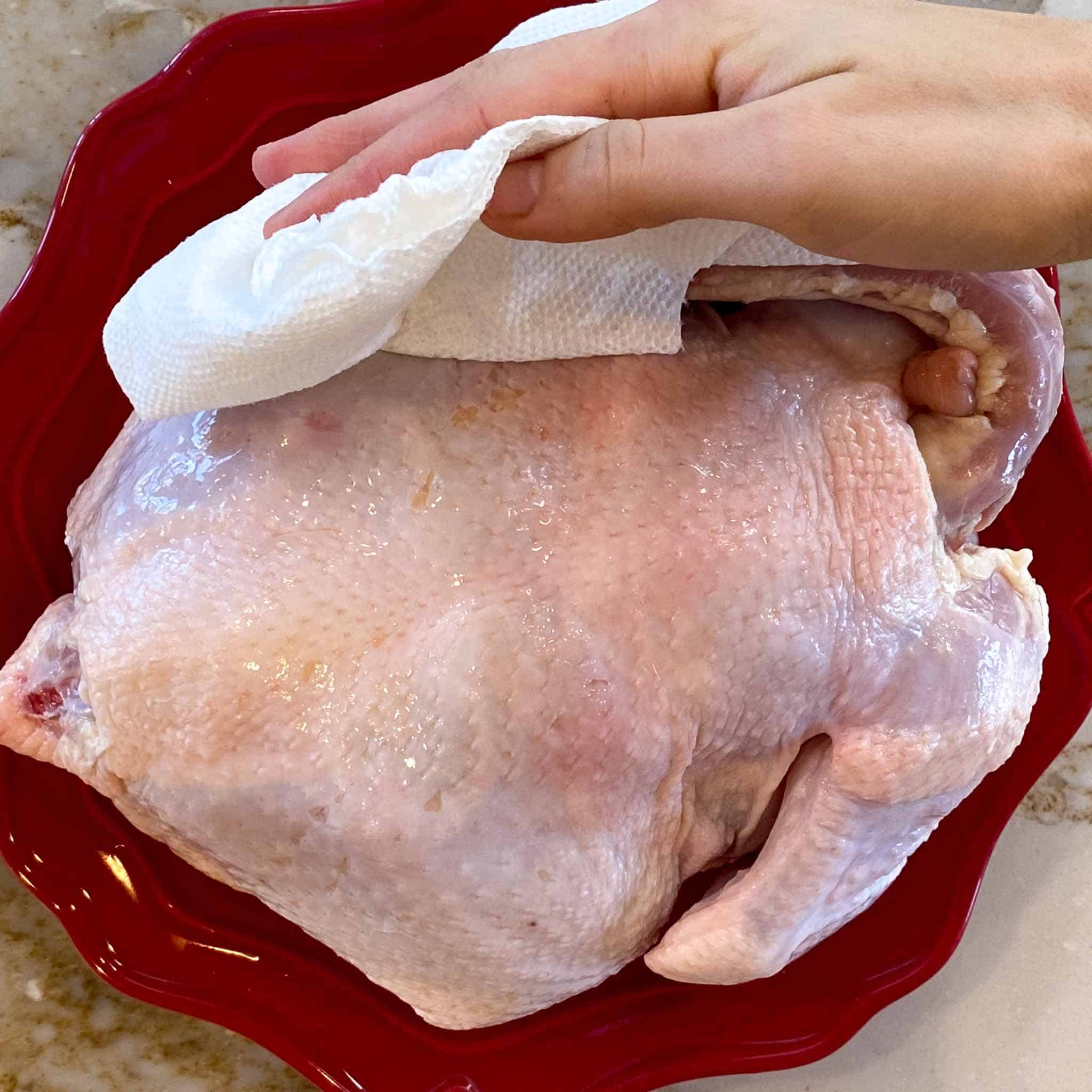 Chicken being patted dry with paper towel.