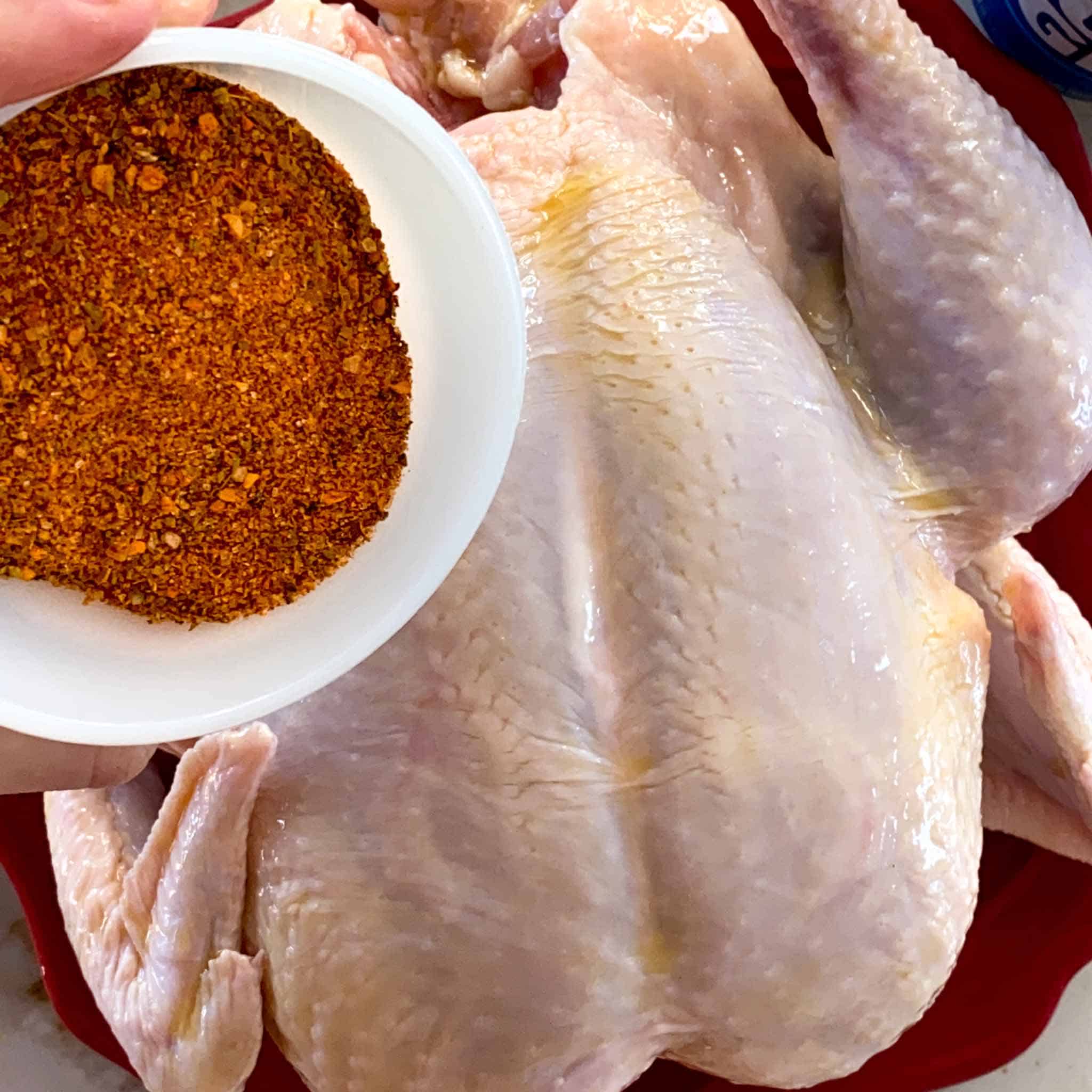 Chicken rub being poured onto a raw chicken, ready to go into the smoker.