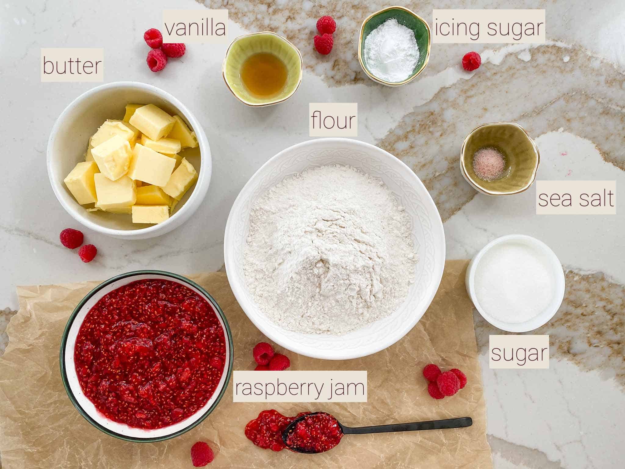 Key ingredients for raspberry crumble cookies spread on the counter including butter, flour, and raspberry jam.