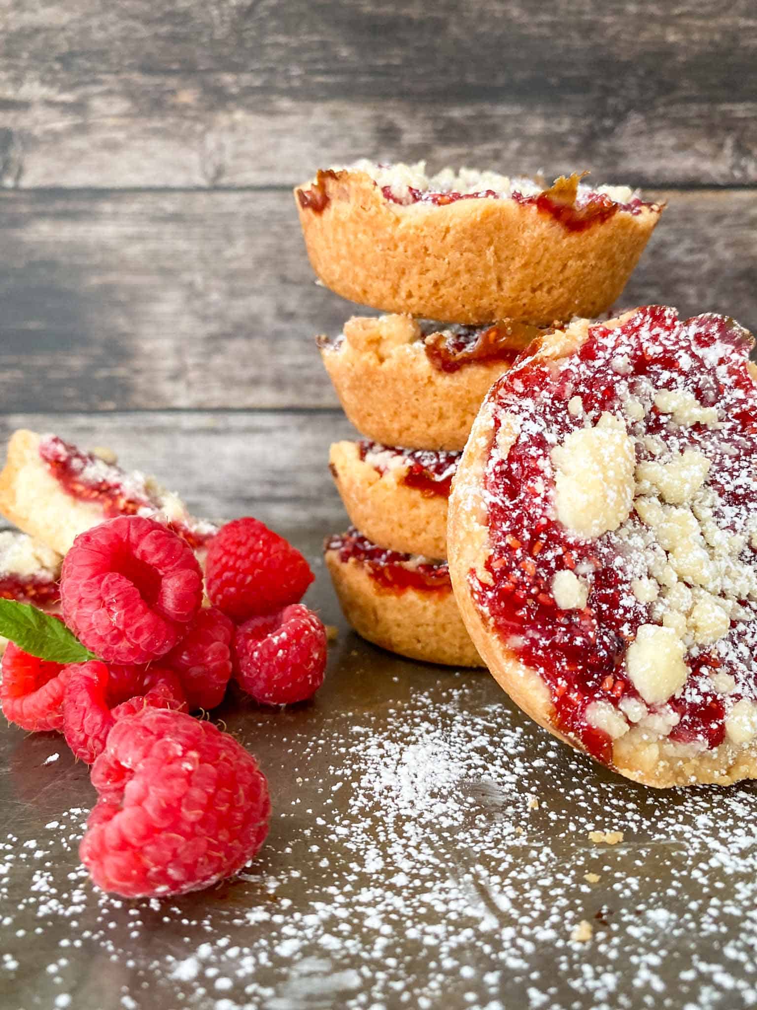 Costco copycat raspberry crumble cookies stacked in a pile with fresh raspberries and icing sugar.