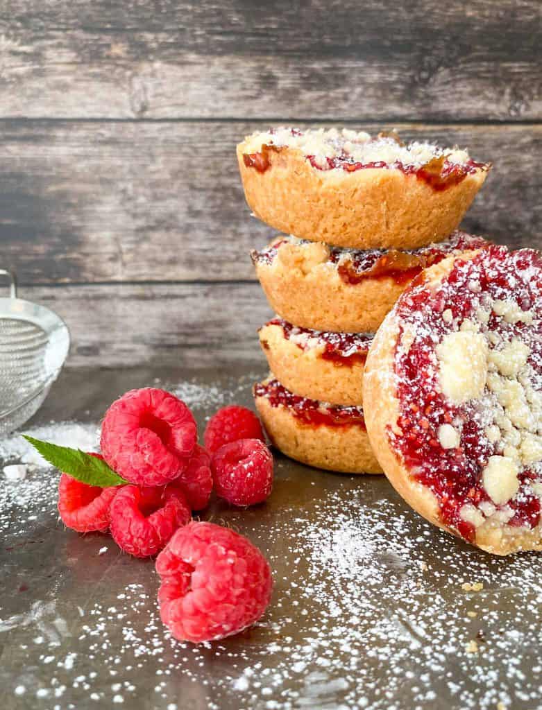 Costco copycat raspberry crumble cookies stacked in a pile with fresh raspberries and icing sugar.