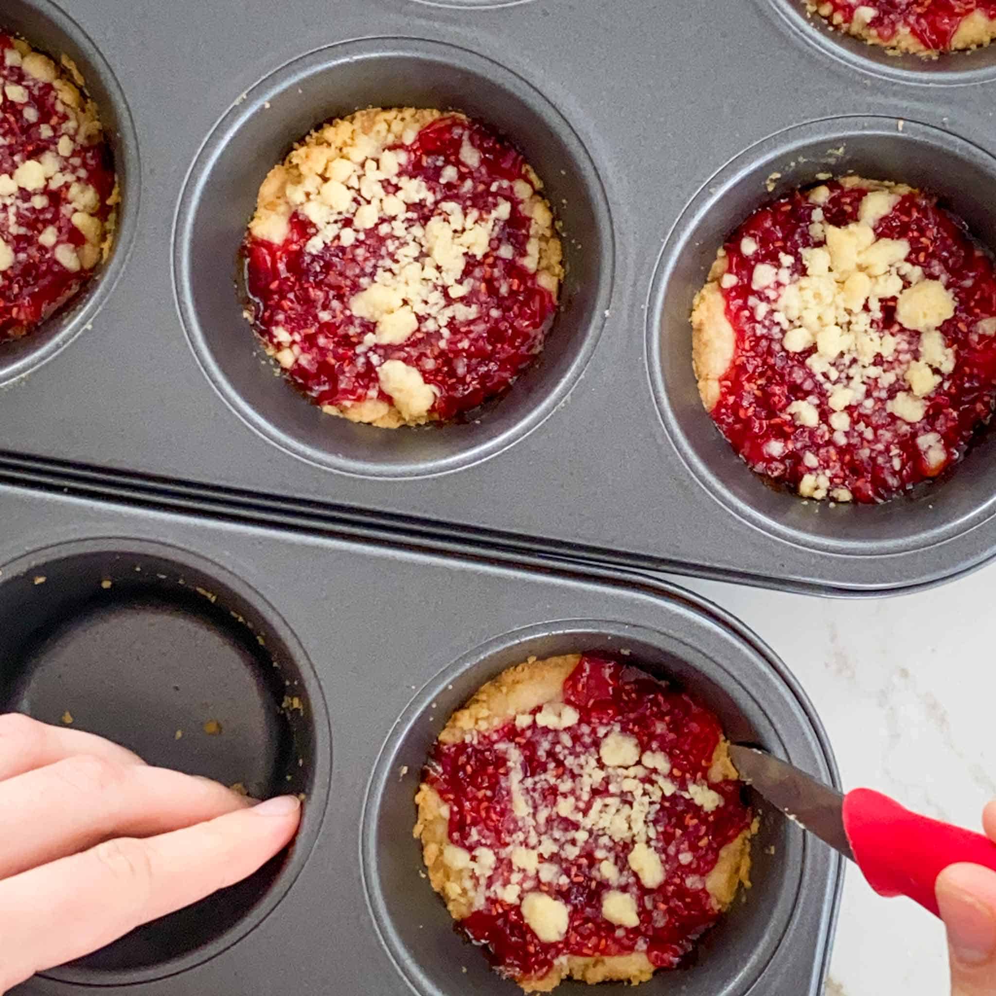 Cooked raspberry crumble cookies being loosened out of muffin tins.