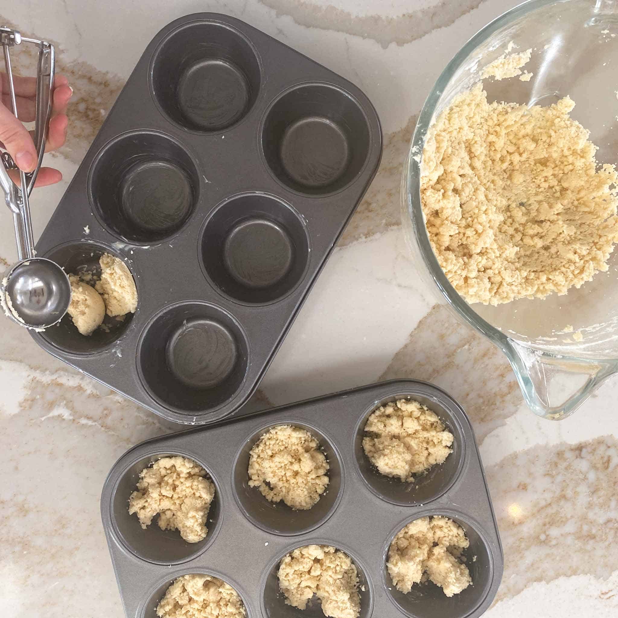 crumble base being spooned into jumbo muffin tins.