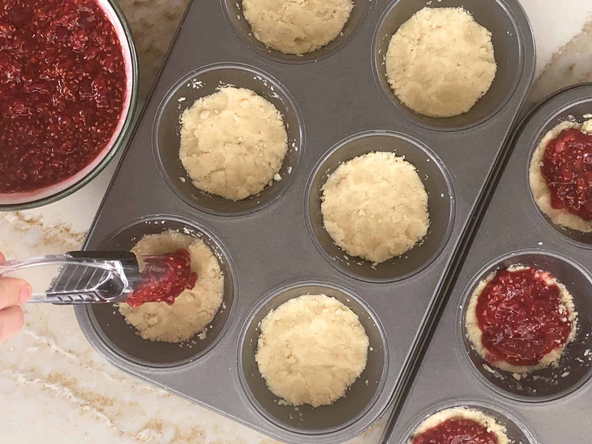 Raspberry jam being spread on the raw crumble cookies.