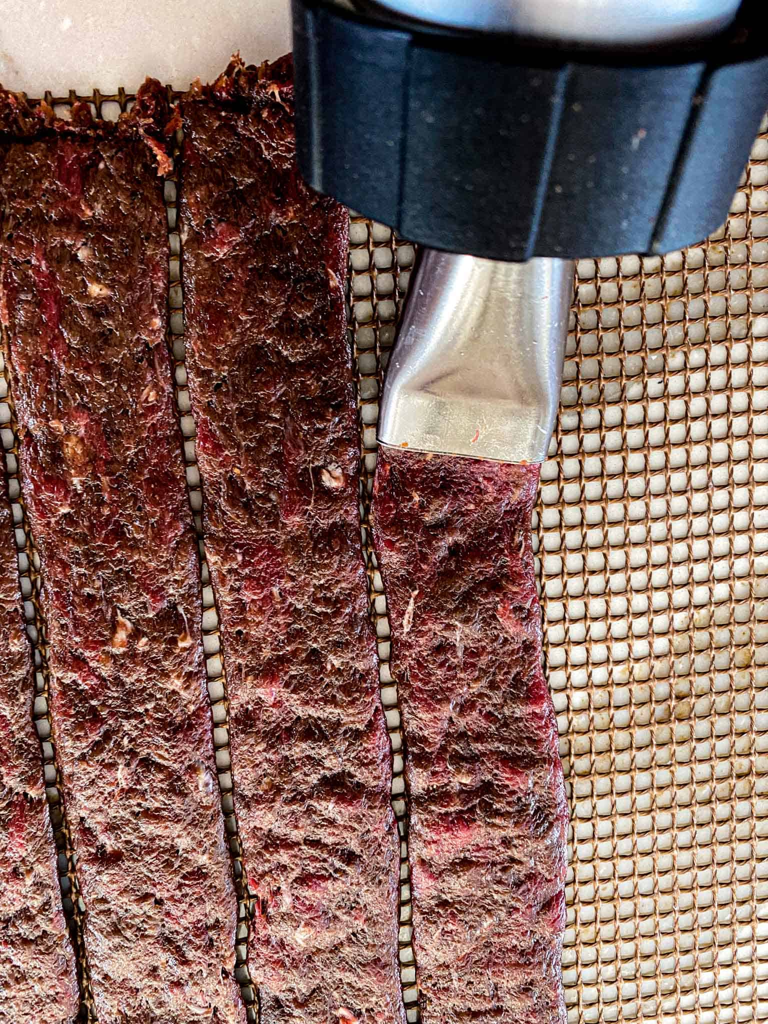 Homemade goose jerky being pressed onto grilling mats with a jerky press.