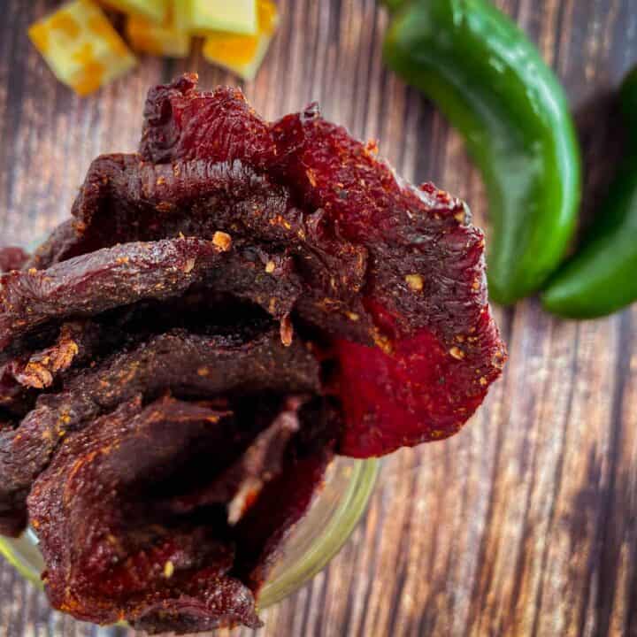 Sliced goose jerky with jalapenos and cheese in the backround on a wooden backdrop.