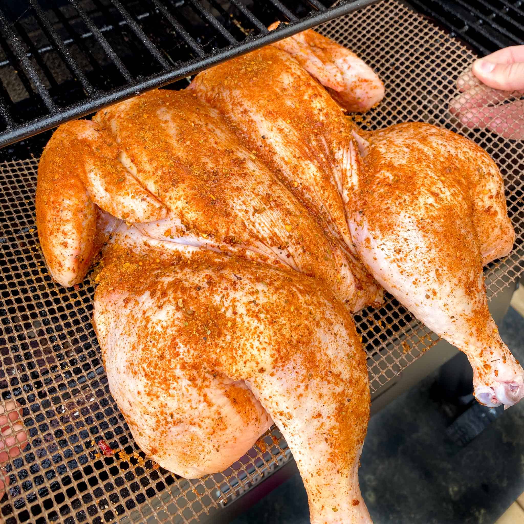 Spatchcock chicken on a grilling mat being put onto a traeger pellet grill.