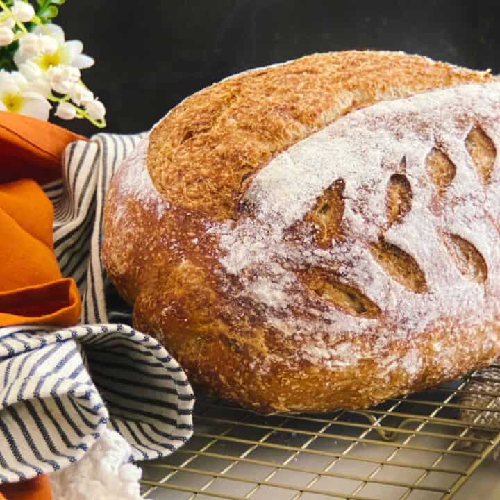 Wholegrain Sourdough Bread on a metal rack, surrounded by an orange and striped napkin and some flowers.