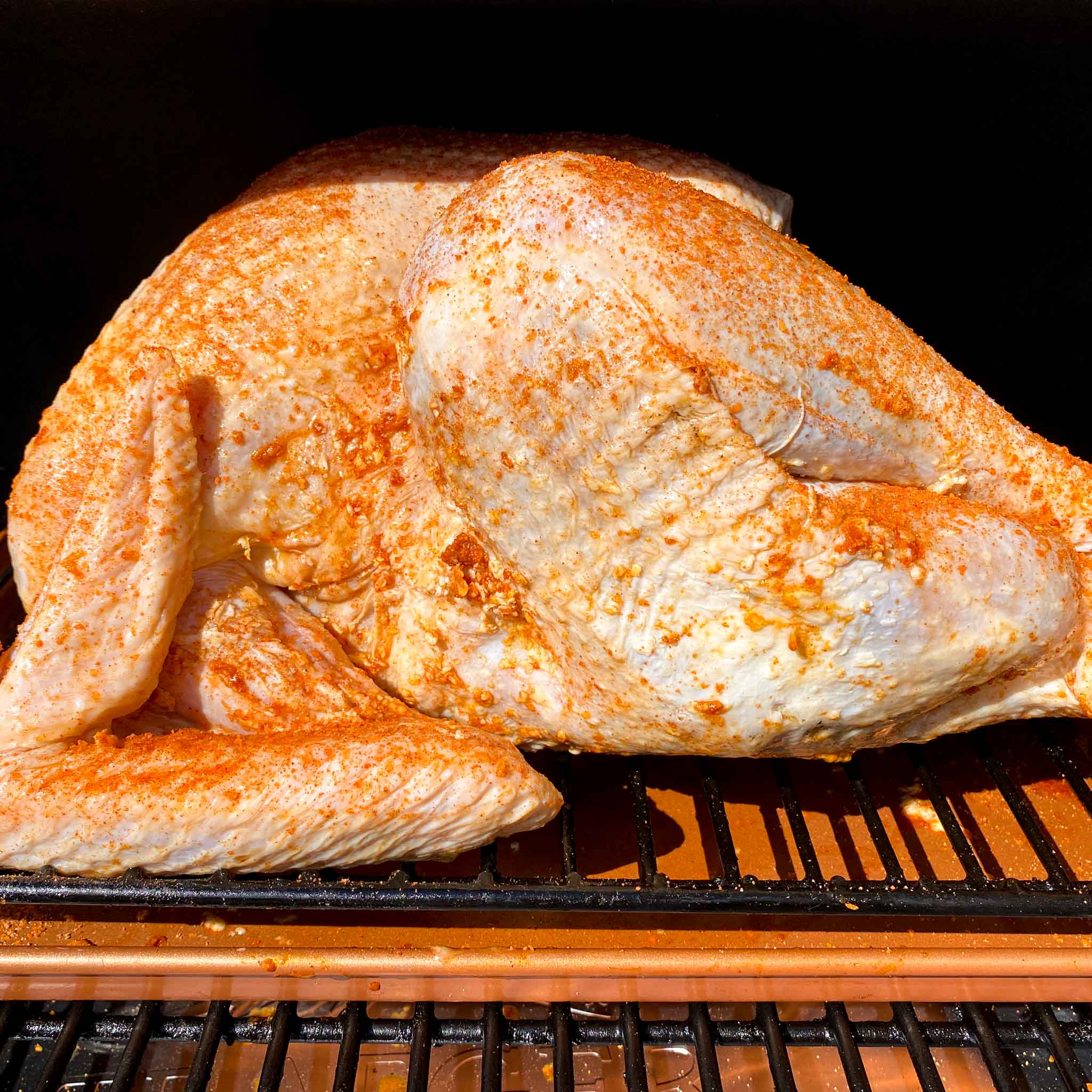 Raw seasoned turkey sitting on a traeger grill, ready to be smoked.