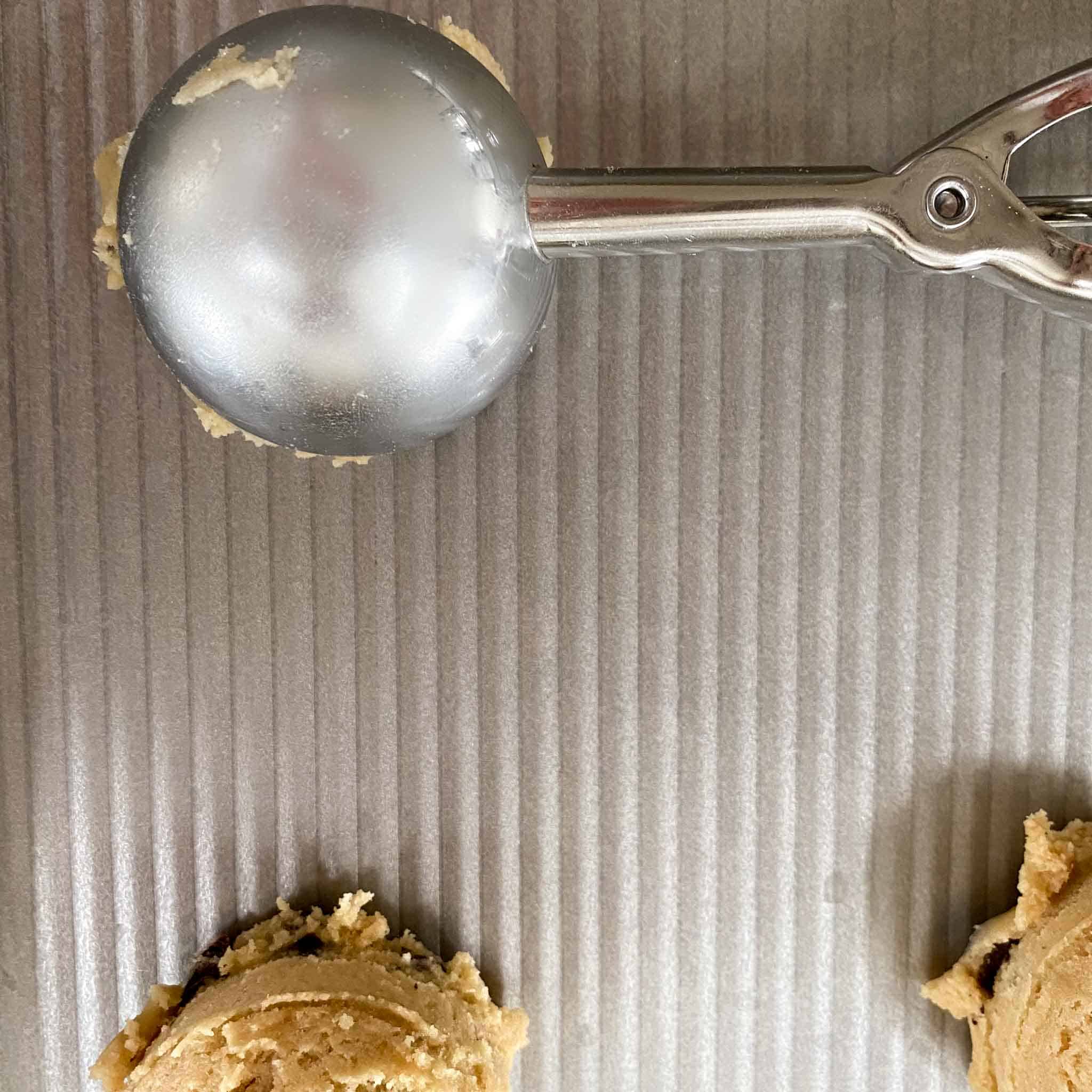 Large cookie scoop dropping chocolate chip cookies without butter on a cookie sheet.