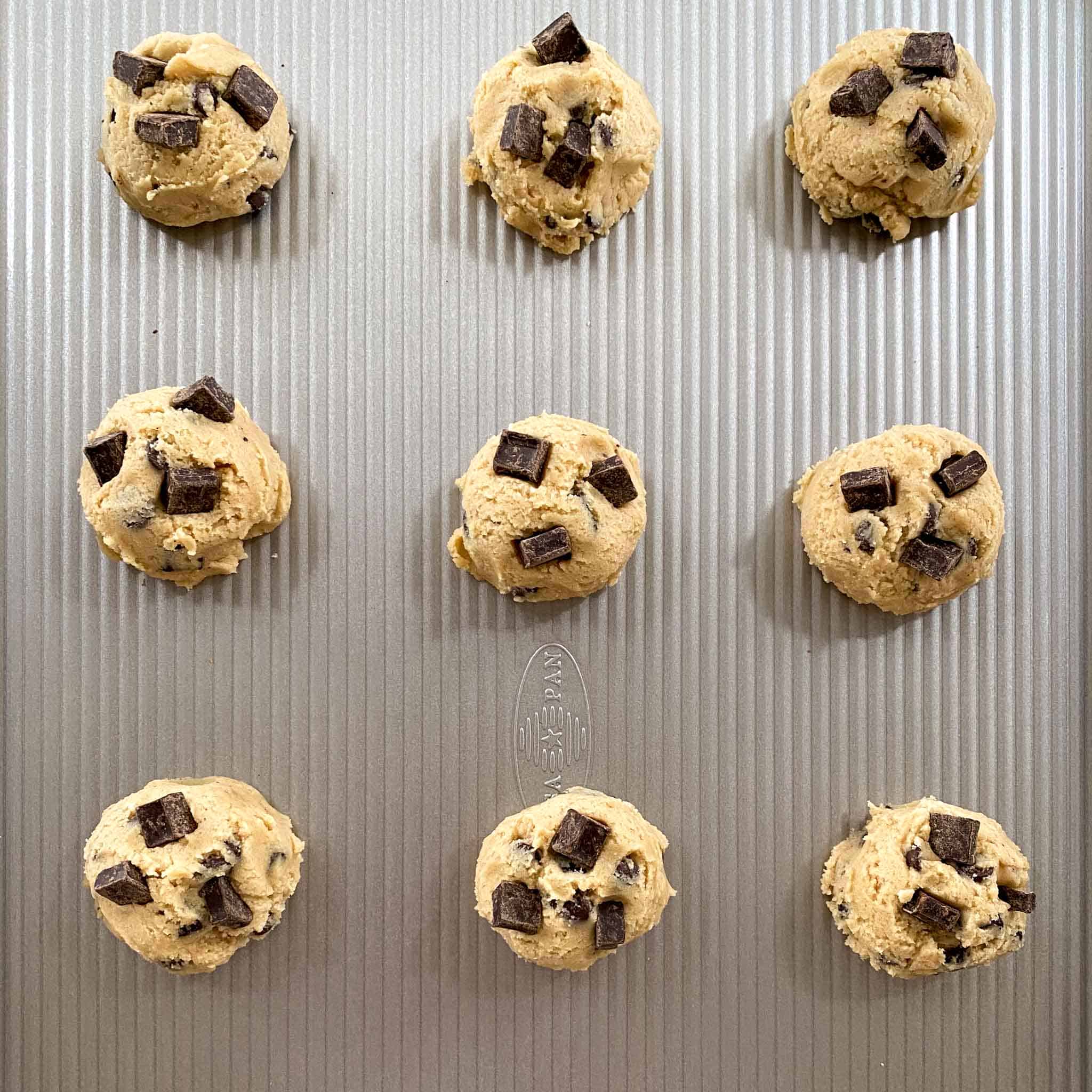 Chocolate chip cookies without butter dropped onto a cookie sheet, ready to be baked.