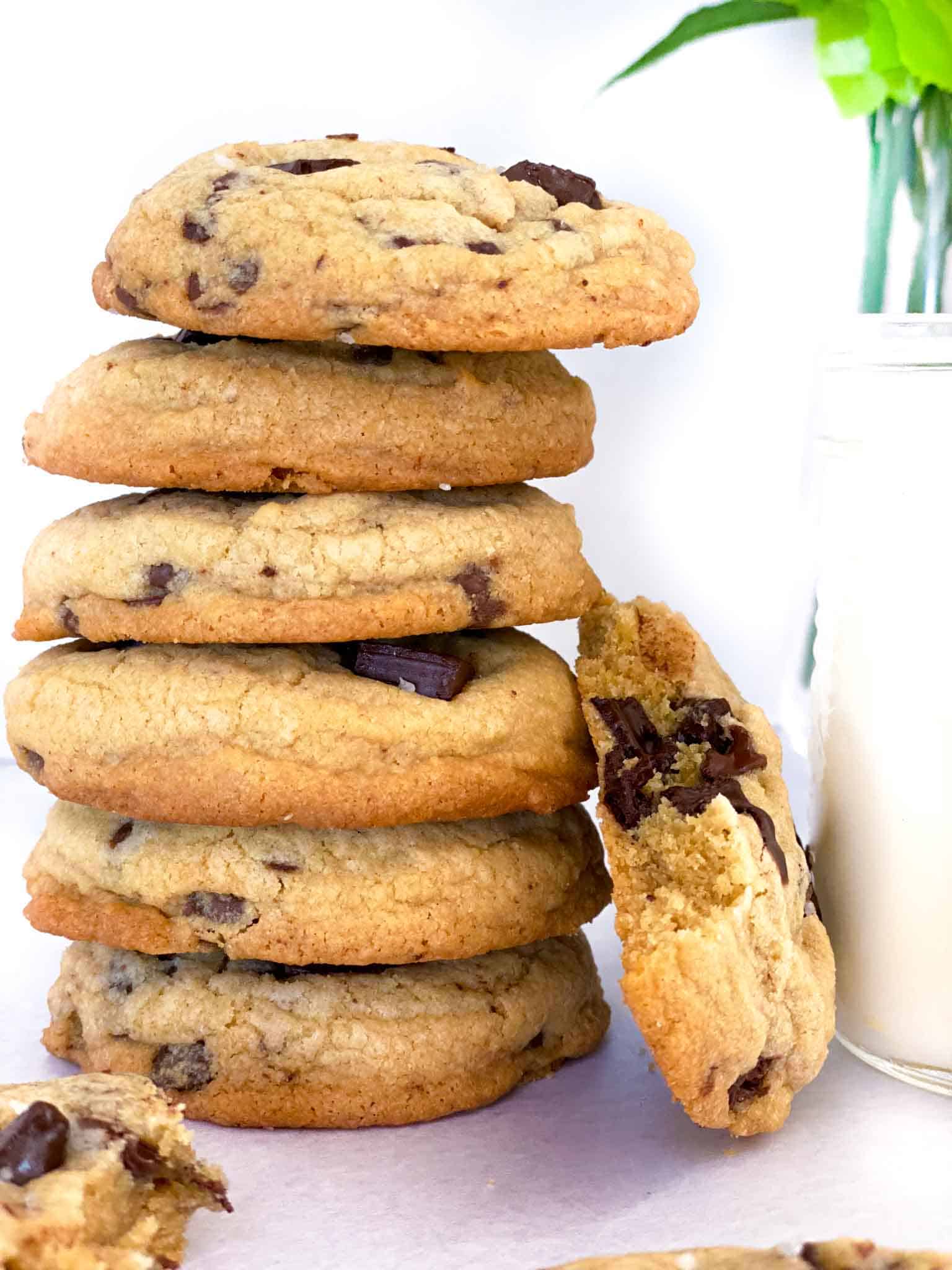 Six chocolate chip cookies without butter stacked on top of each other with a glass of milk next to it.