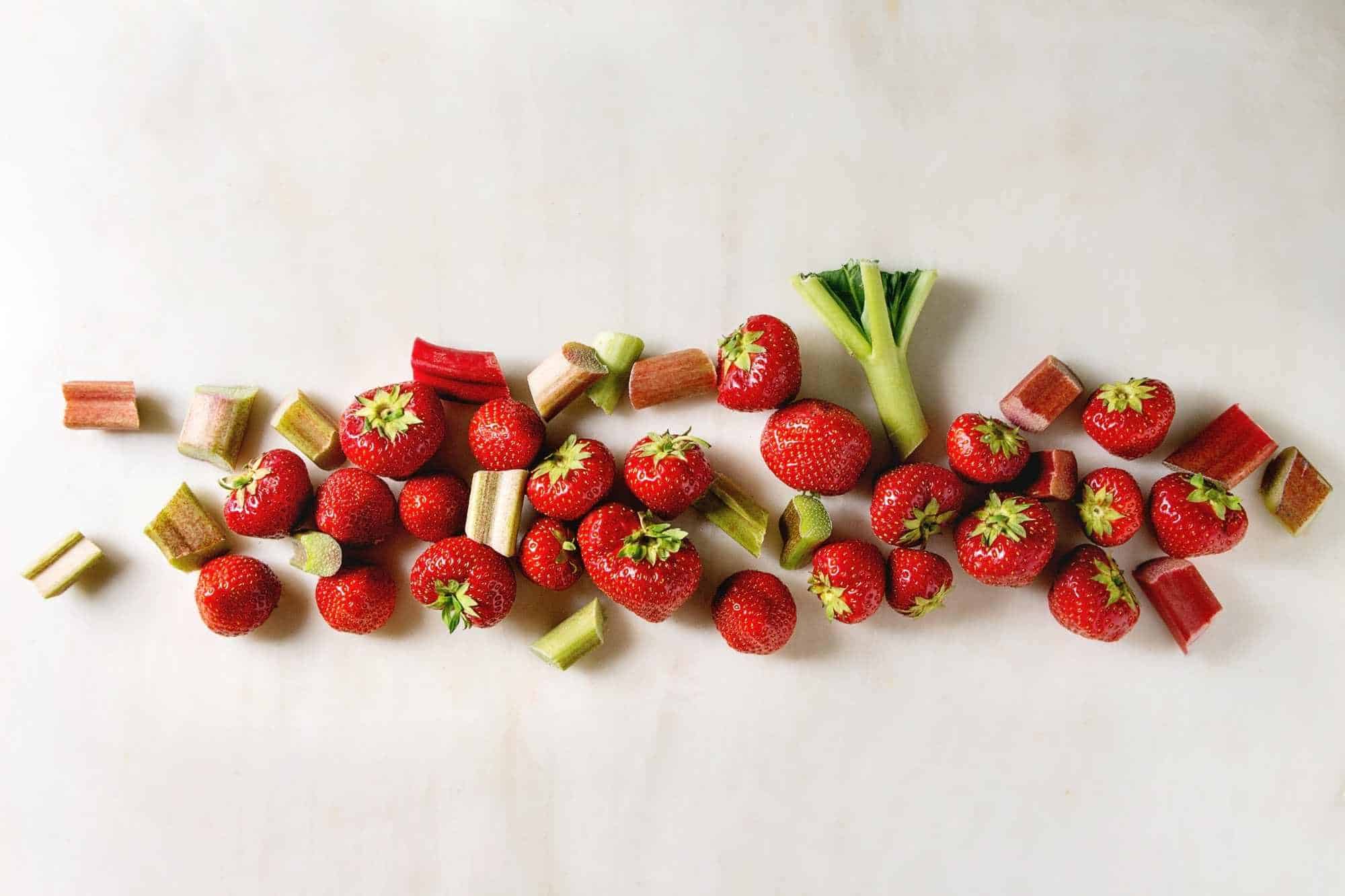 Strawberries and Rhubarb companion plants chopped up in a line on a white backdrop.