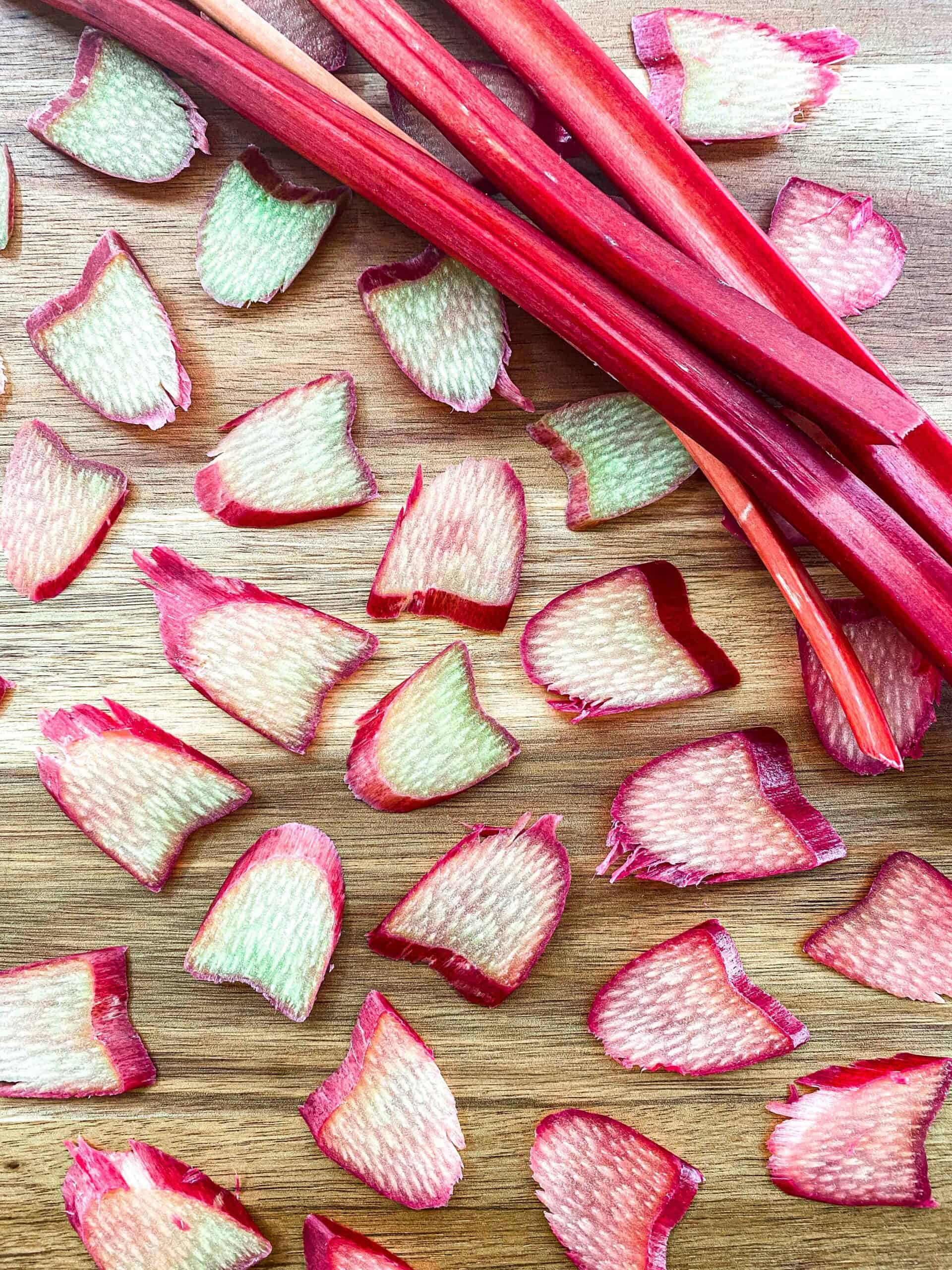 Thinly sliced rhubarb medallions with rhubarb stocks on a wooden backdrop.