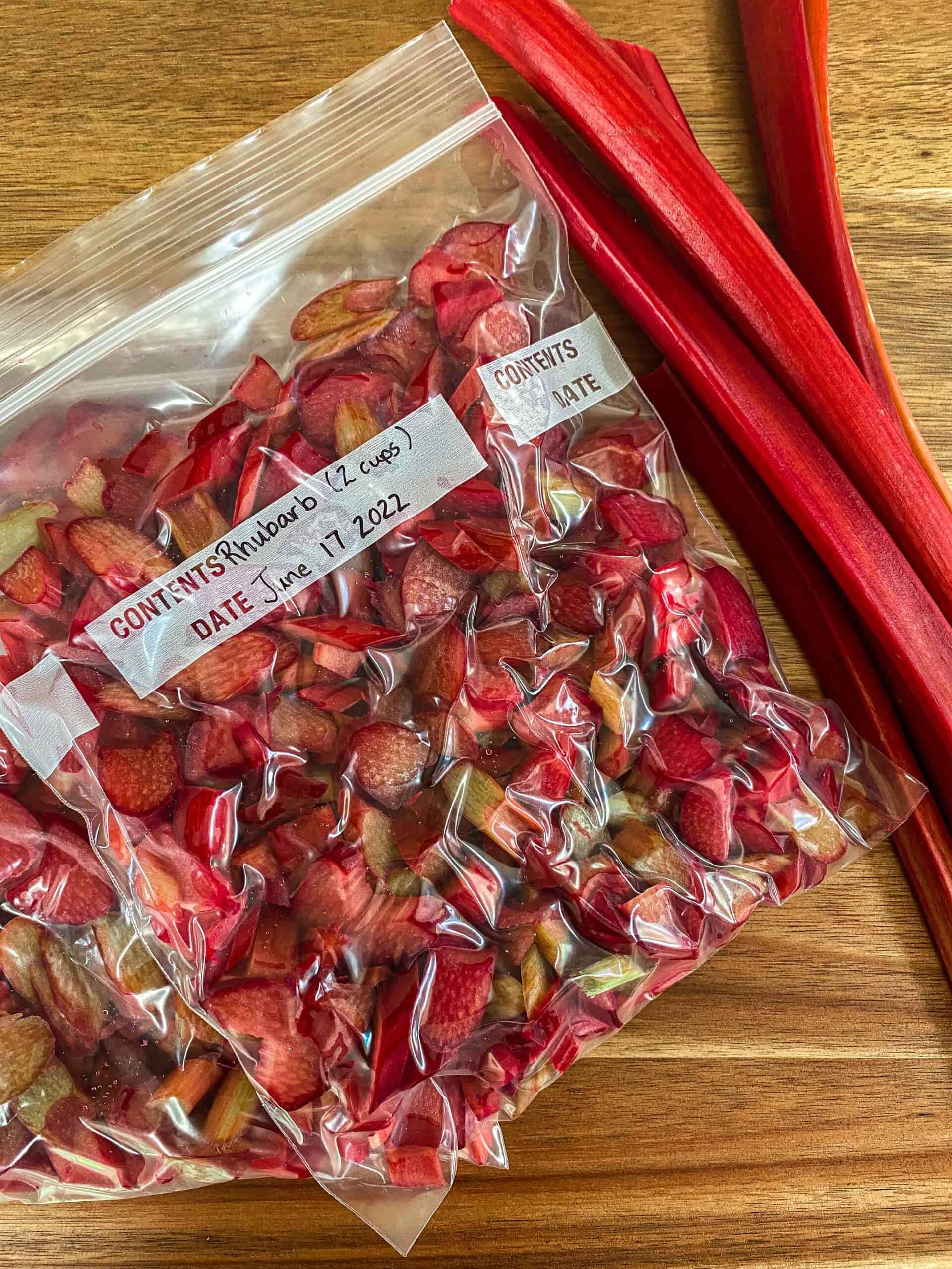 Frozen rhubarb in two freezer bags cut up with three stalks of rhubarb laying beside.