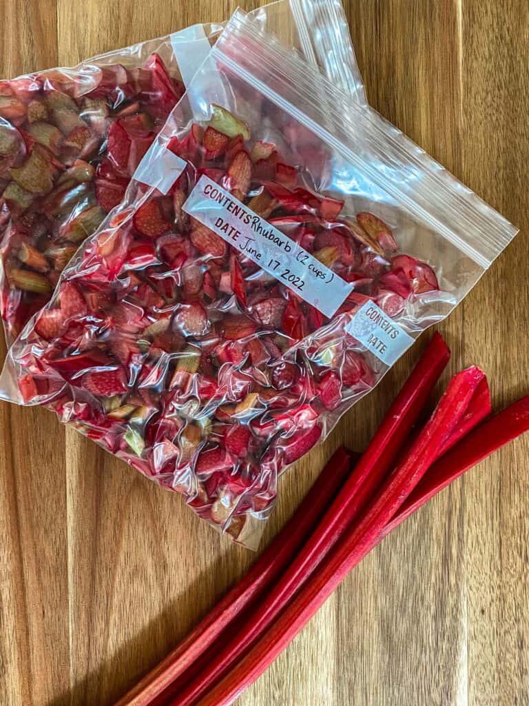 Frozen rhubarb in two freezer bags cut up with three stalks of rhubarb laying beside.
