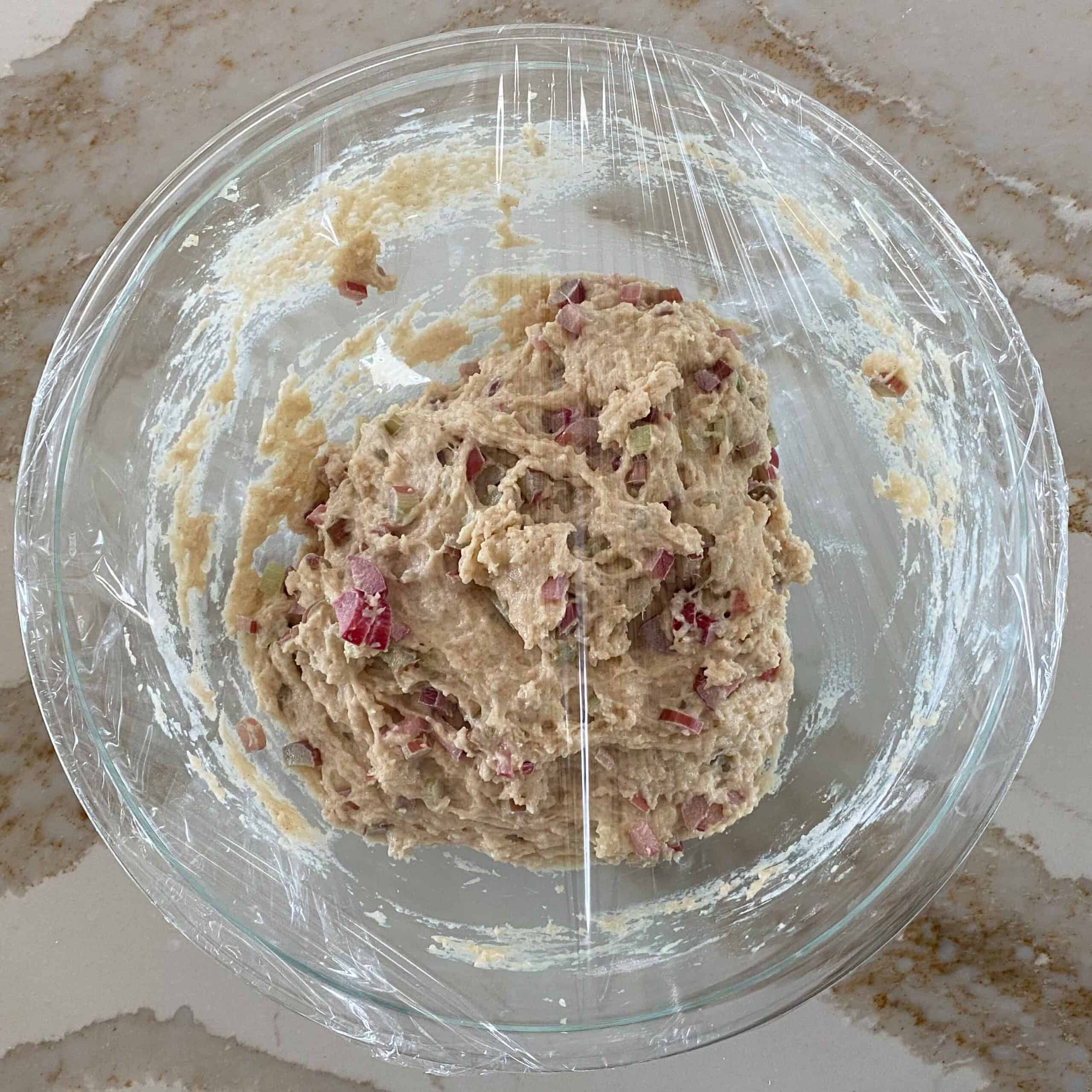Rhubarb muffin batter in a covered glass bowl, ready to be chilled.