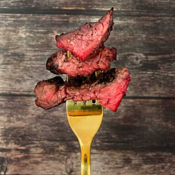 Smoked tri tip roast showing perfectly pink insides on a golden fork with a wooden backdrop.
