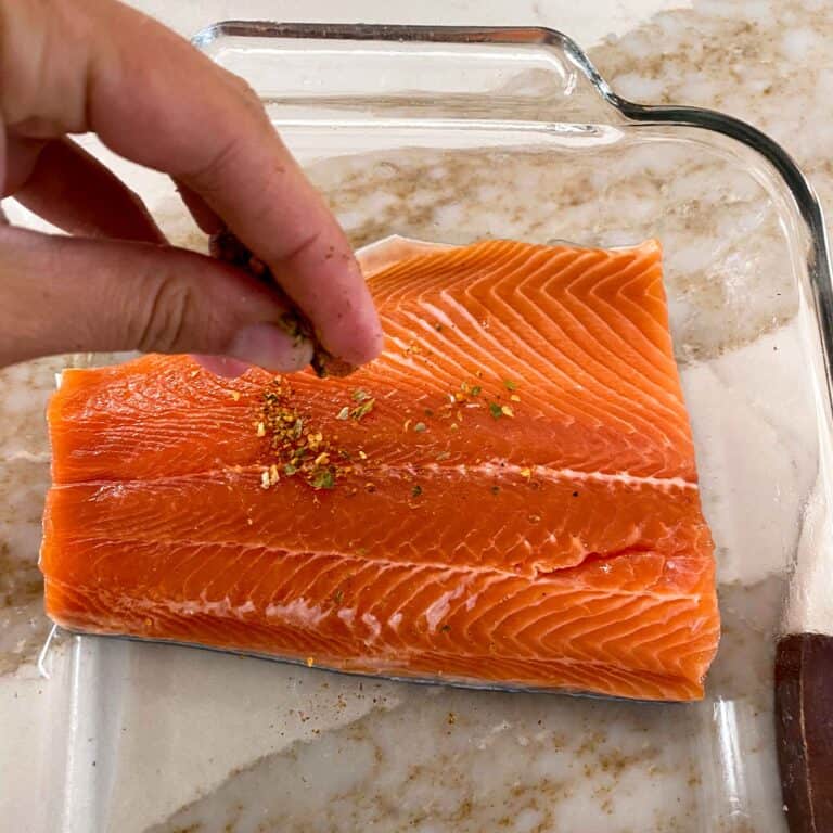 Sprinkling dry rub onto a raw trout fillet.