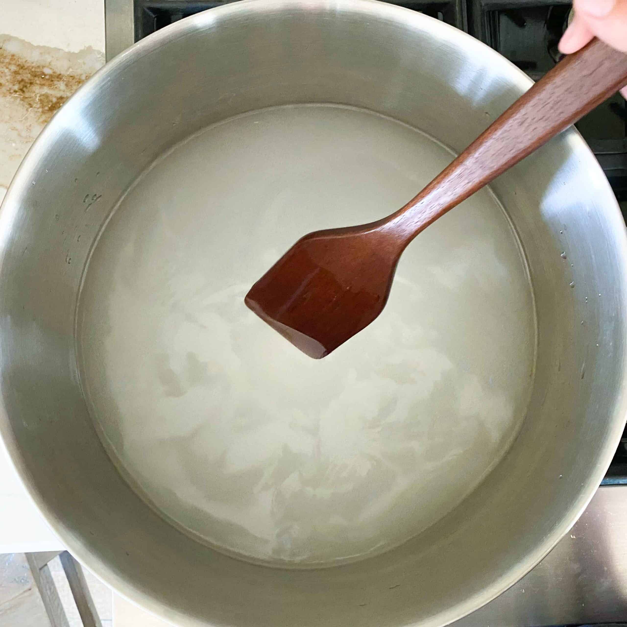 Wooden spatula stirring a large pot of brine for fermented dill pickles.