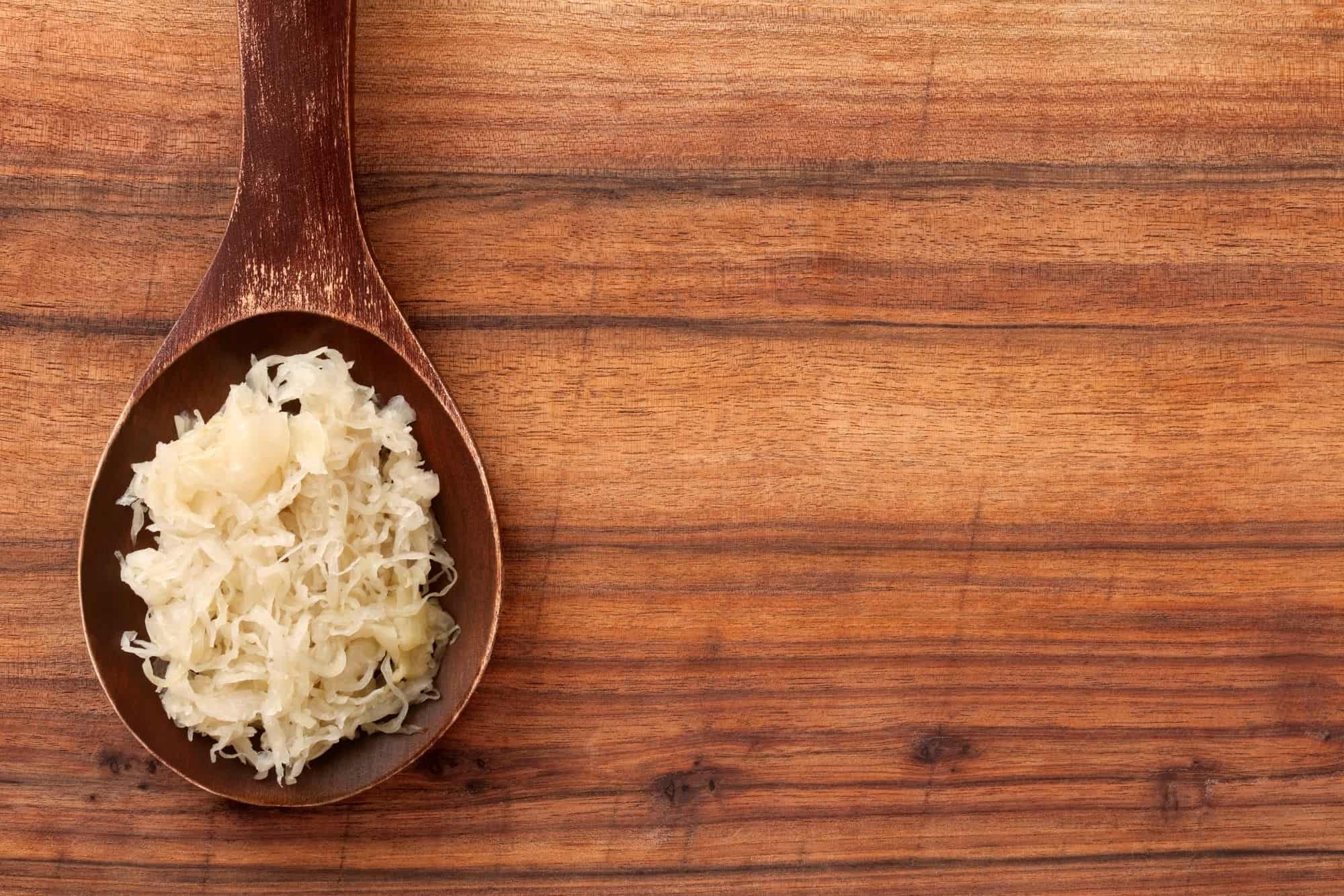 Sauerkraut on a wooden spoon with a wooden backdrop.