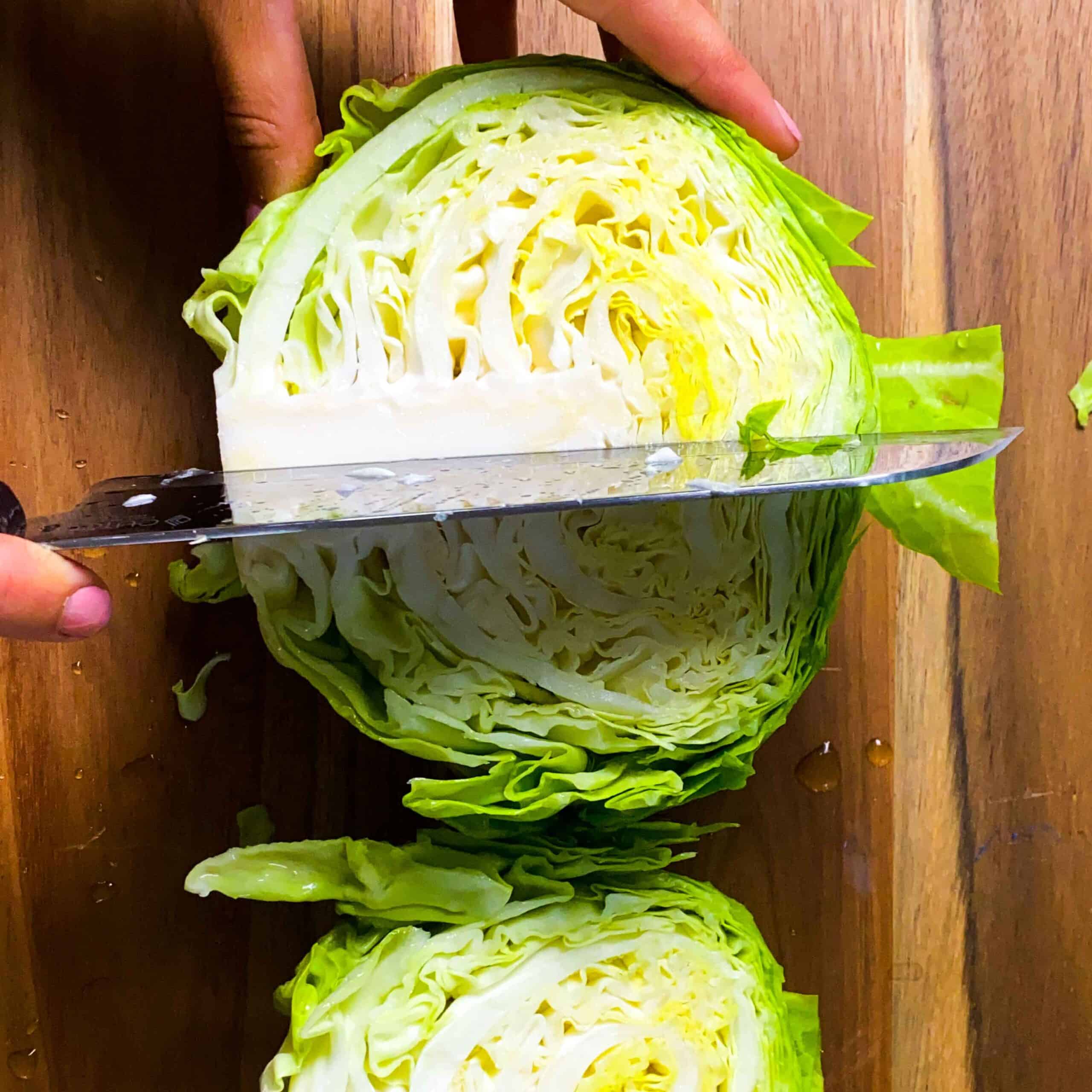 Whole cabbage head being cut in quarters on a wooden cutting board.