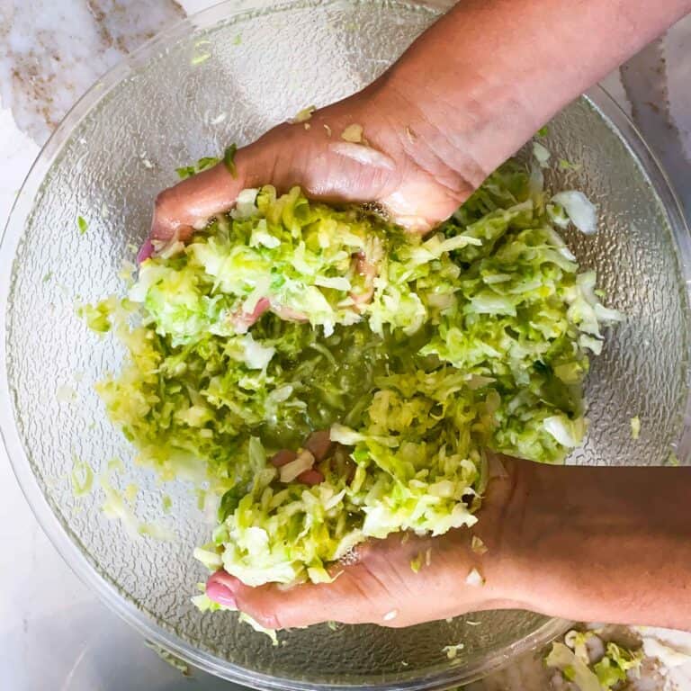 Shredded cabbage being massaged in a large mixing bowl.