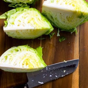 Wedged cabbage with a large knife over a wooden cutting board.