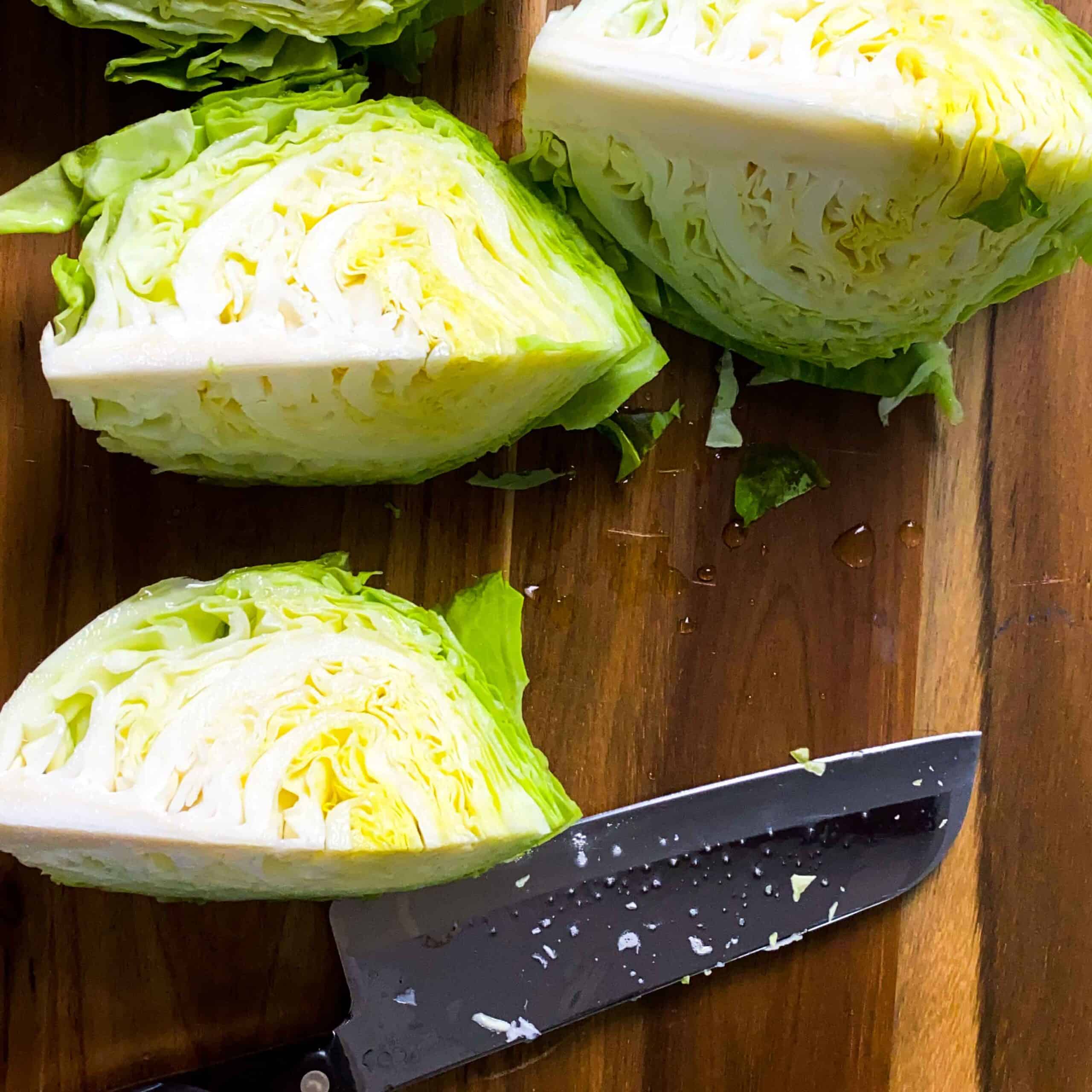 Wedged cabbage with a large knife over a wooden cutting board.