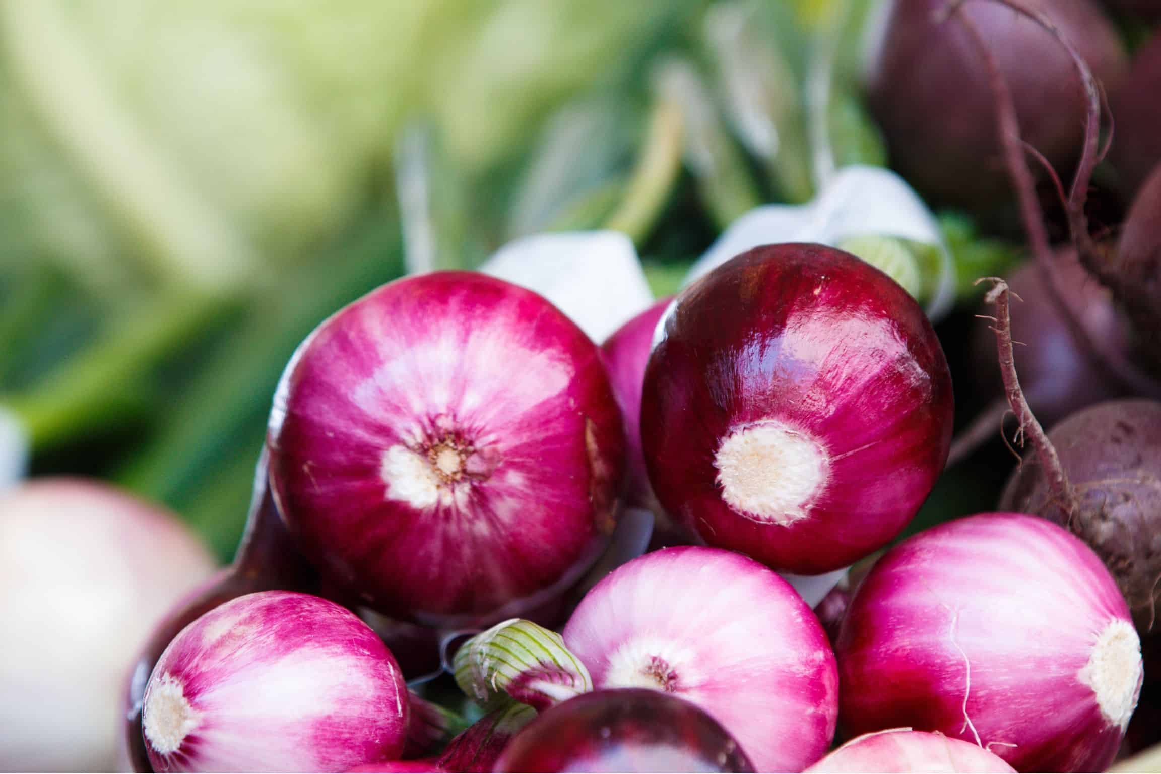 Purple onions stacked on top of one another with green stems blurred in the back.