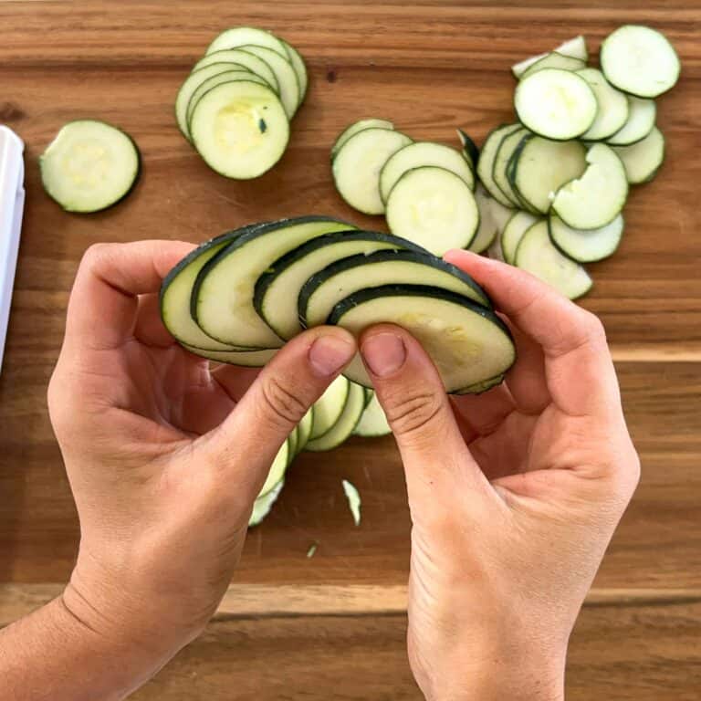 A sideways view of sliced zucchini chips being held in between hands to show slice thickness.
