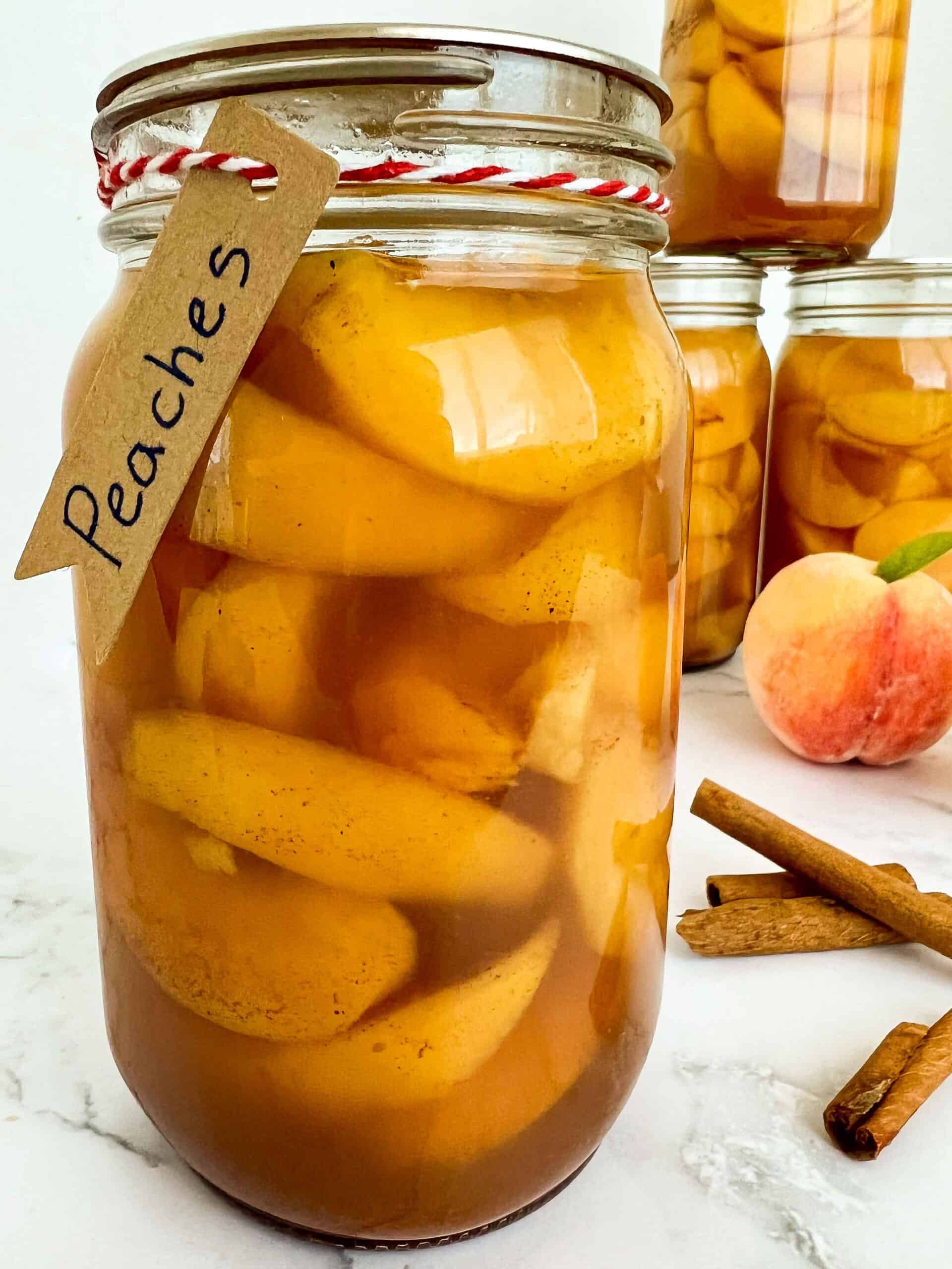 Canned peaches with brown sugar and spices in a jar with a brown paper label and red and white butcher twine.